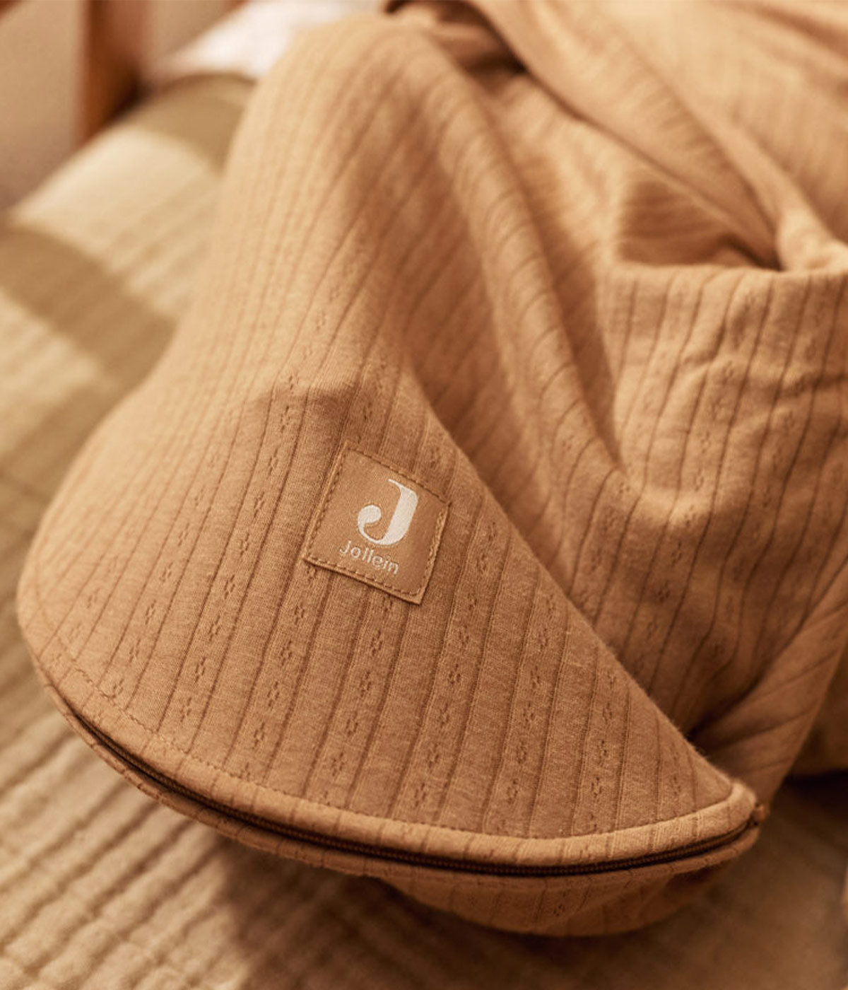 Swaddle wrap castanho marca Jollein com detalhes na malha para bebé e recém-nascido(a), 100% algodão. Composta por abas com velcro, este swaddle wrap oferece um ajuste suave e seguro, adaptando-se delicadamente ao corpo do bebé.