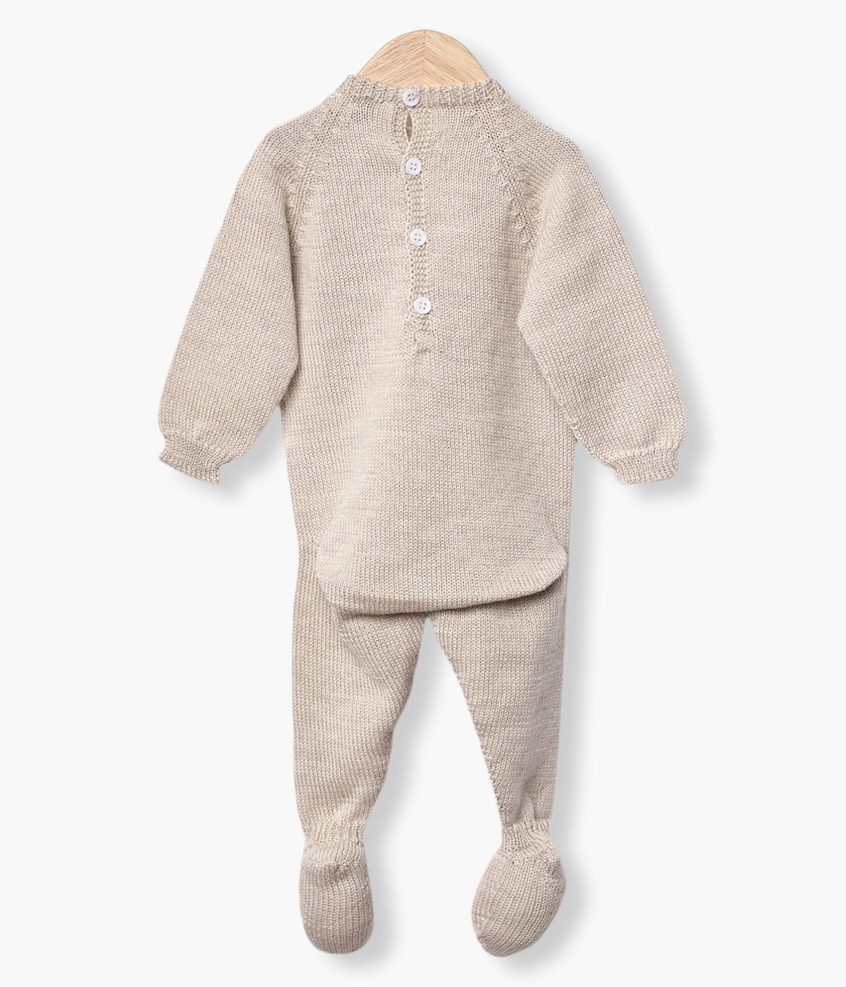 Babygrow tricotado em lã merino bege da Wedoble para bebé e recém-nascido(a). Quentinho babygrow com detalhes entrelaçados na malha. Abertura nas costas e entrepernas.