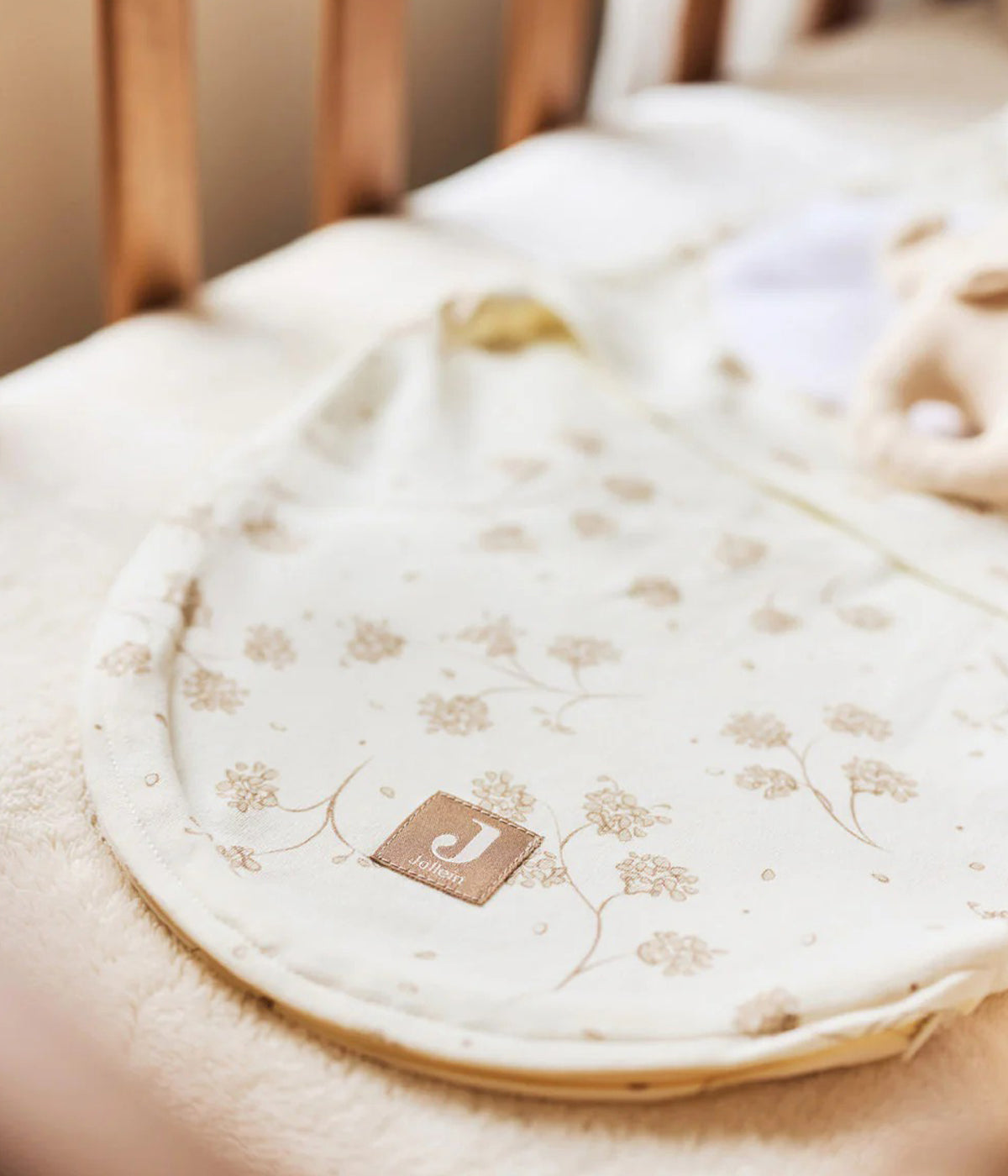 Swaddle wrap pérola marca Jollein com padrão dentes-de-leão em tons de bege para bebé e recém-nascido(a), 100% algodão. Composto por abas com velcro, este swaddle wrap oferece um ajuste suave e seguro, adaptando-se delicadamente ao corpo do bebé.