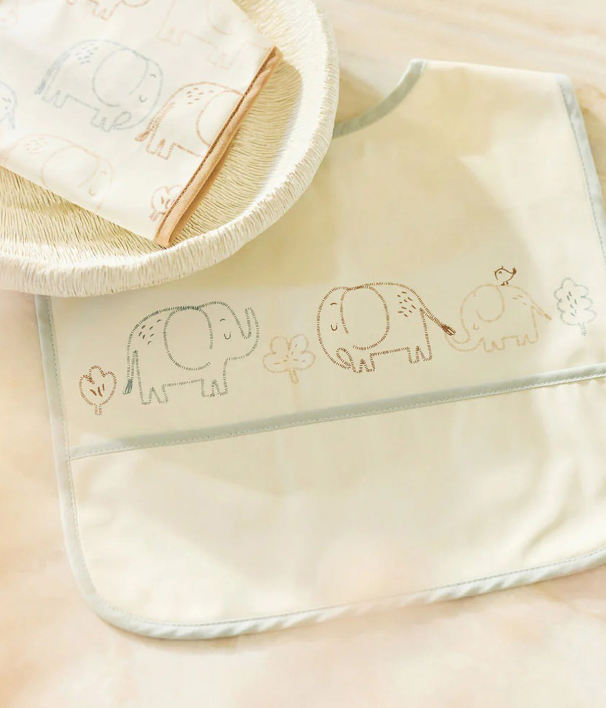 Conjunto de duas babetes impermeáveis pérola com padrão elefantes em tons de azul e bege da Jollein para bebé e recém-nascido(a). Babetes impermeáveis com bolso perfeitas para manter o bebé limpo enquanto aprende a beber e comer sozinho.