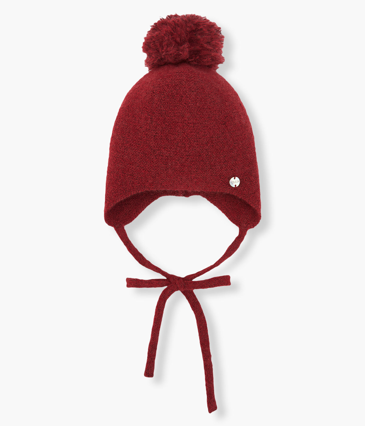 Gorro em malha com lã da Paz Rodríguez para bebé e recém-nascido(a). Pompom à cor, medalha madrepérola com logo da marca e tiras para atar no queixo.