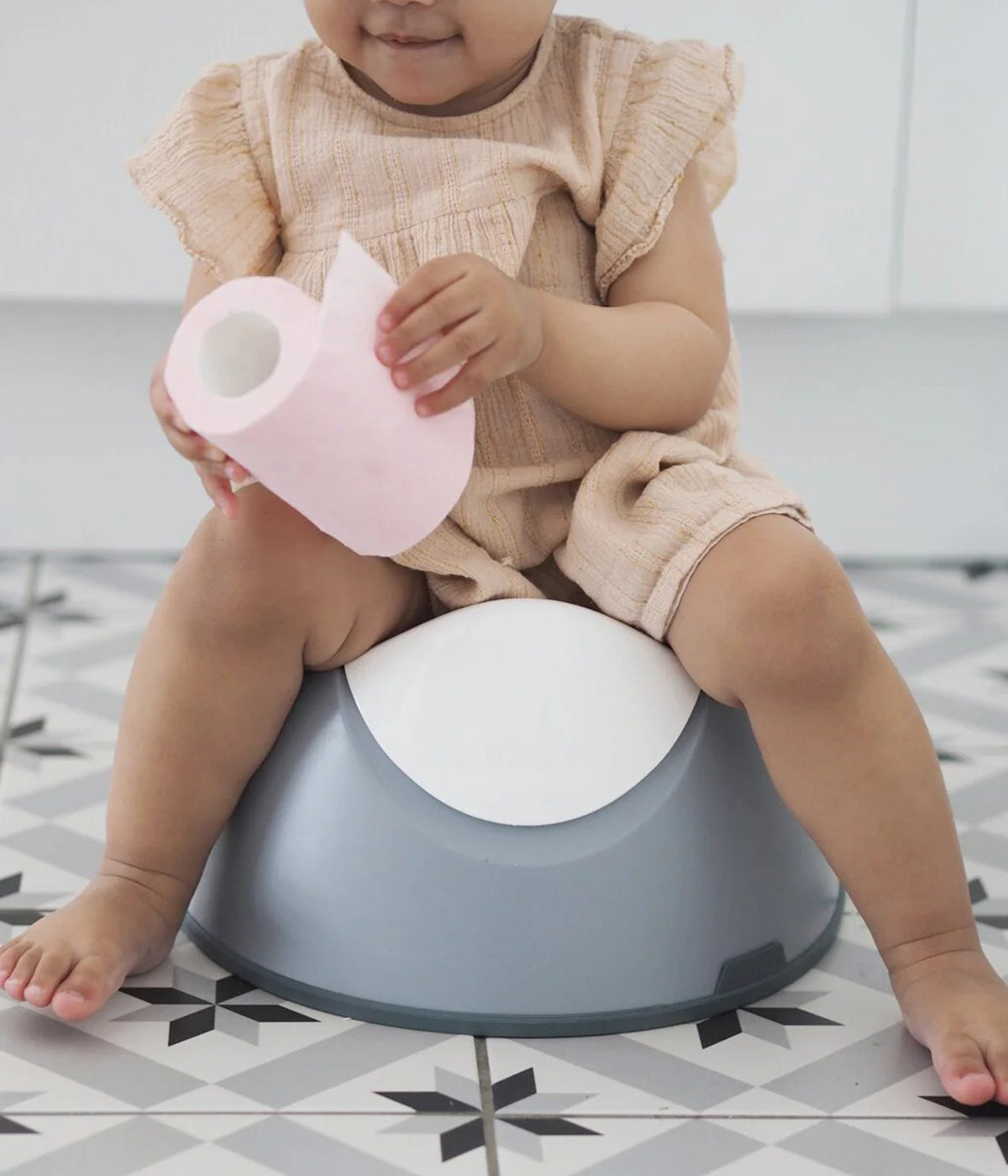 Vista frontal com bebé a utilizar do bacio ergonómico Potty da Béaba na cor Light Mist (cinza).