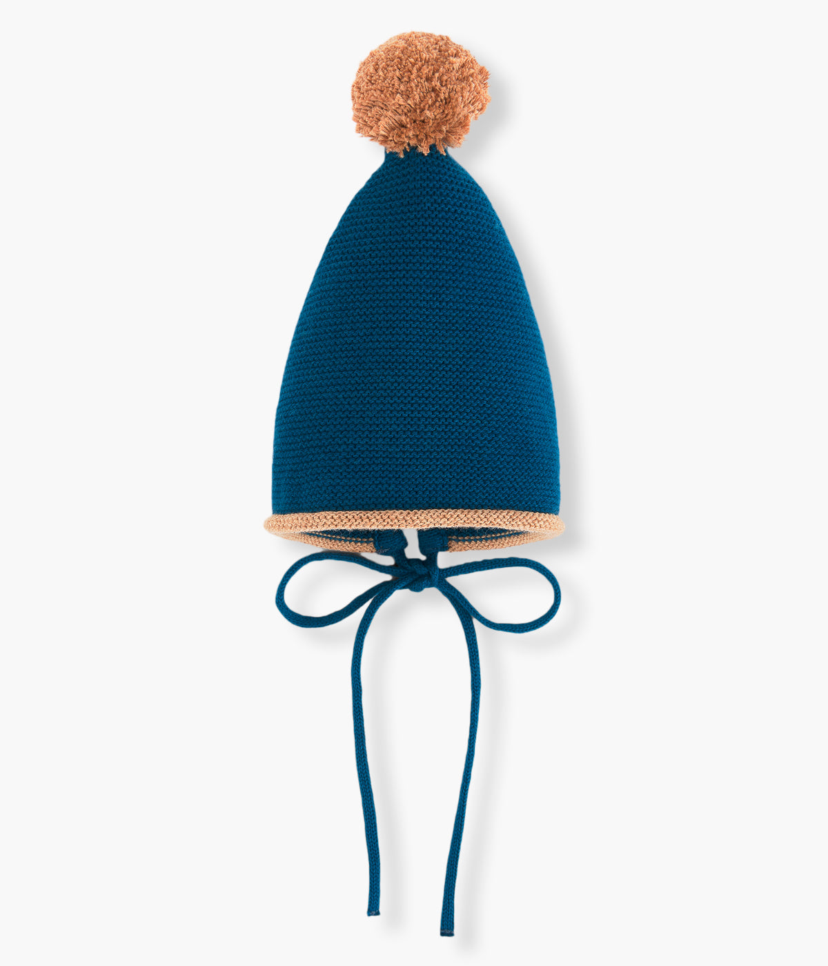 Vista frontal do gorro em malha com algodão da Paz Rodríguez para bebé e recém-nascido(a). Pompom e contorno em bege. Medalha da marca em madeira. Tiras para atar no queixo.