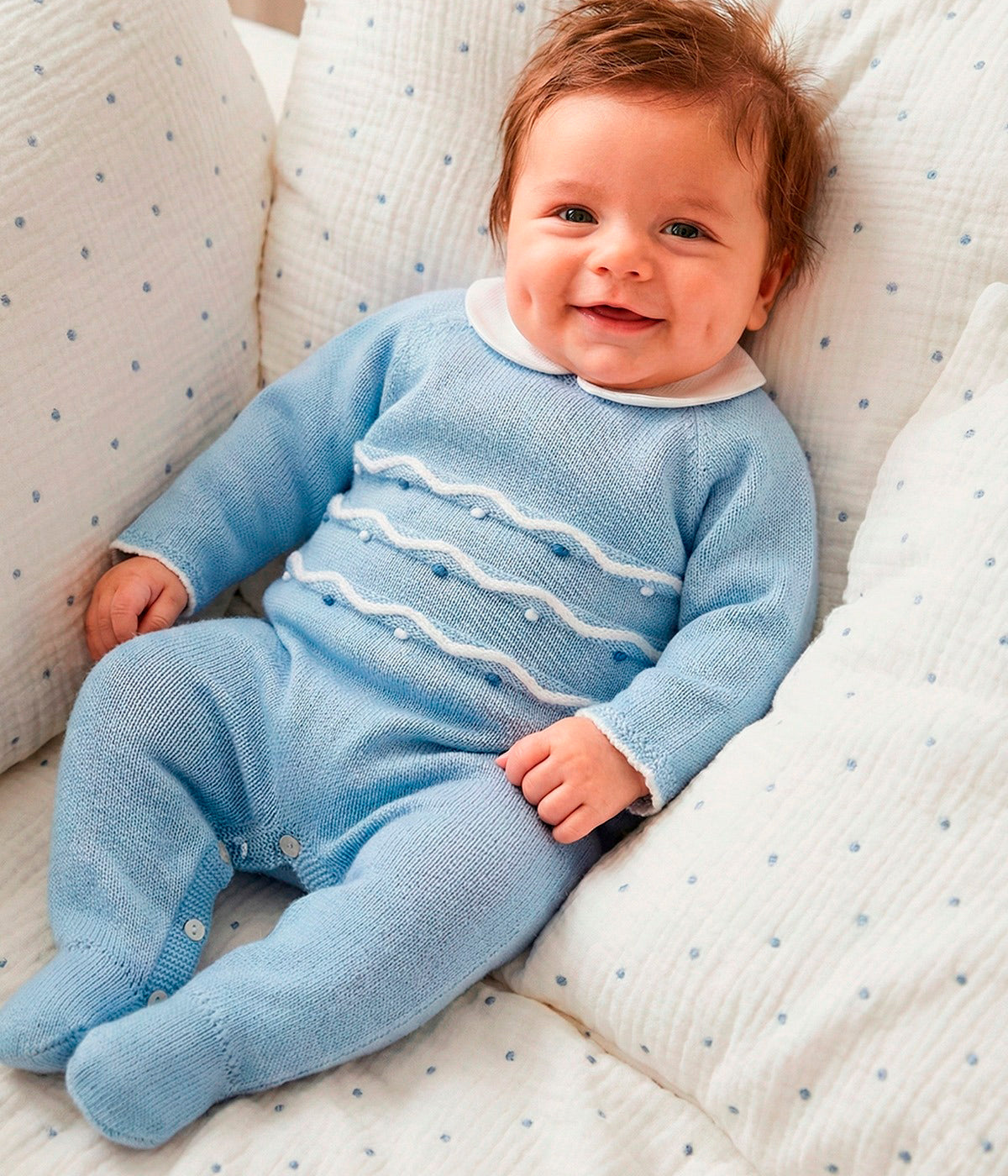 Vista de um bebé a vestir o babygrow em malha azul da Mac Ilusión para bebé e recém-nascido(a). Elegante babygrow sem pés com gola redonda branca e bolinhas e detalhes com relevo em branco e tons de azul. Abertura nas costas e entrepernas.