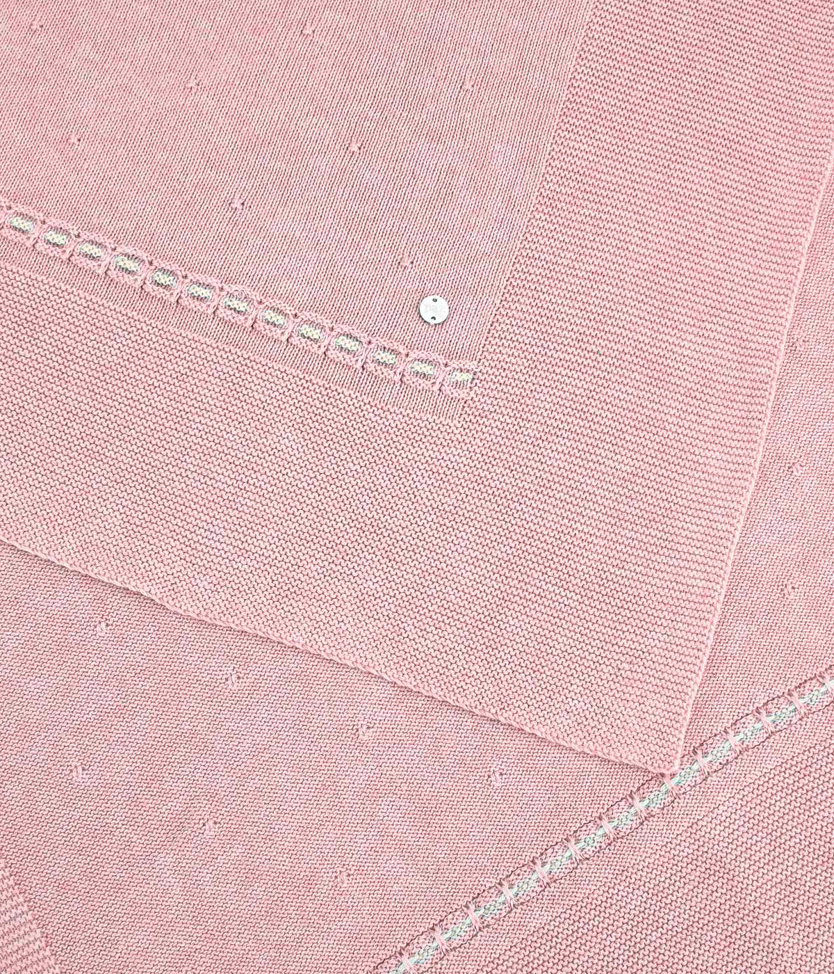 Vista da manta em malha de algodão e caxemira rosa da Paz Rodríguez para bebé menina e recém-nascida. Suave manta de formato retangular com detalhes em bege e medalha de madrepérola.