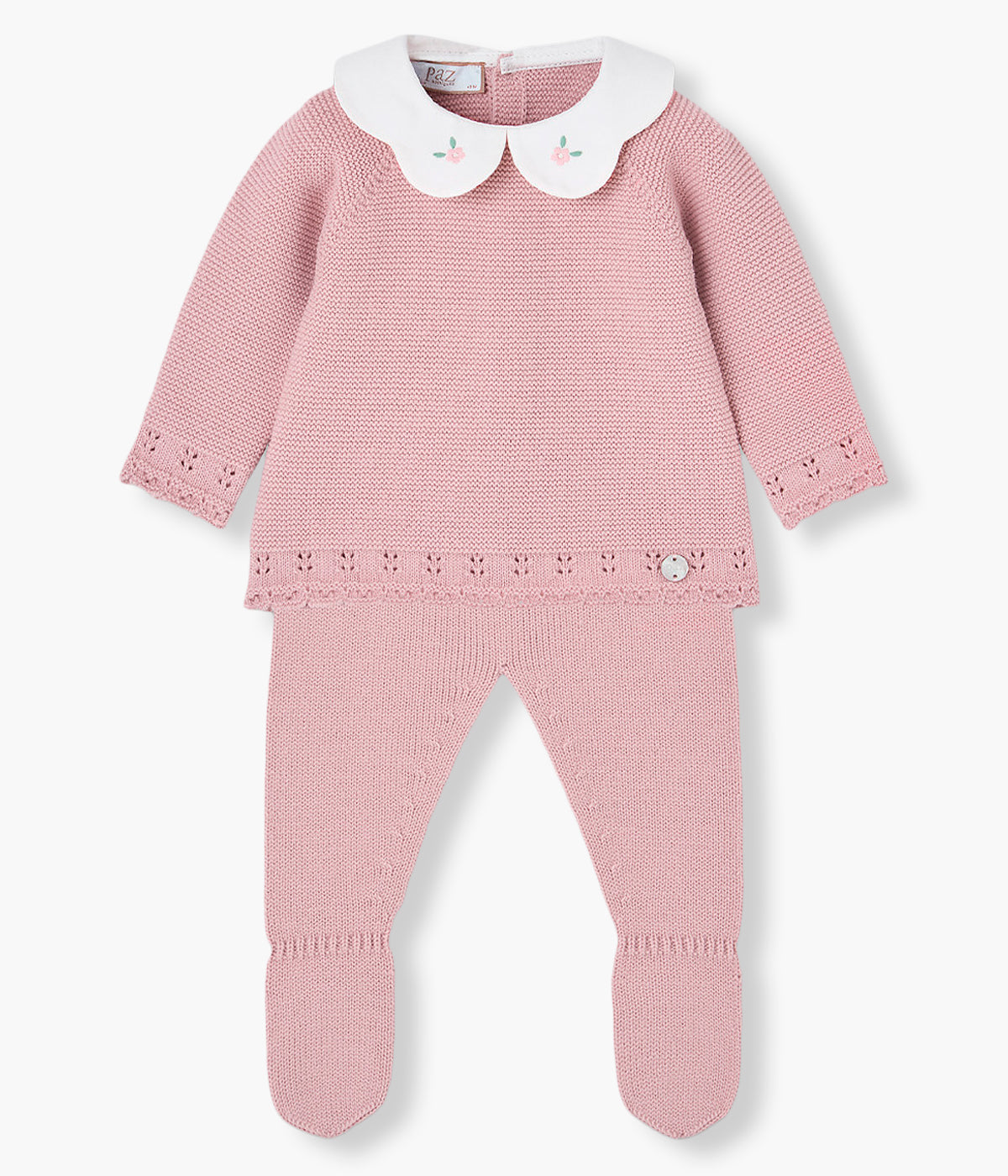 Vista frontal do conjunto de 2pc em malha rosa da Paz Rodríguez para bebé menina e recém-nascida. Camisola com gola redonda cortada em tecido branco com bordado flores e contornos com detalhes perfurados na malha. Calças com pés.