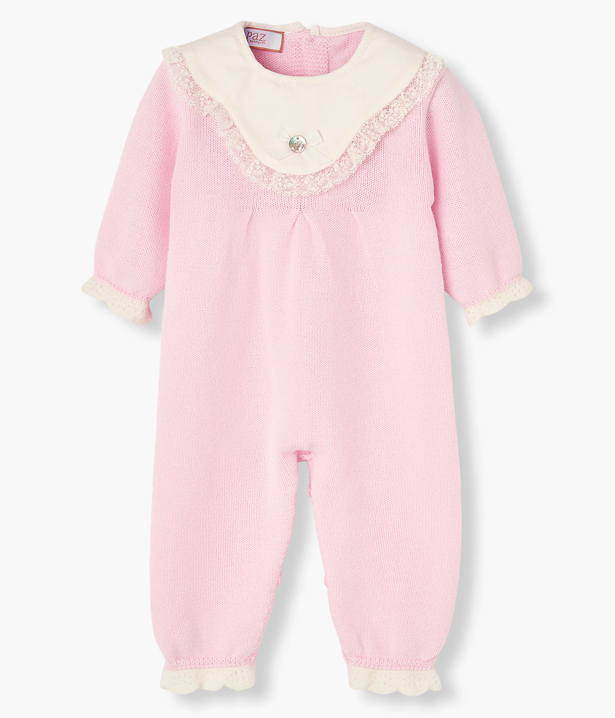 Vista frontal do babygrow em malha rosa da Paz Rodríguez para bebé menina e recém-nascida. Peitilho em tecido branco com rebordo em renda detalhada bege e medalha de madrepérola com laço gorgurão. Extremidades com detalhe ondulado pérola. Abertura nas costas e entrepernas.