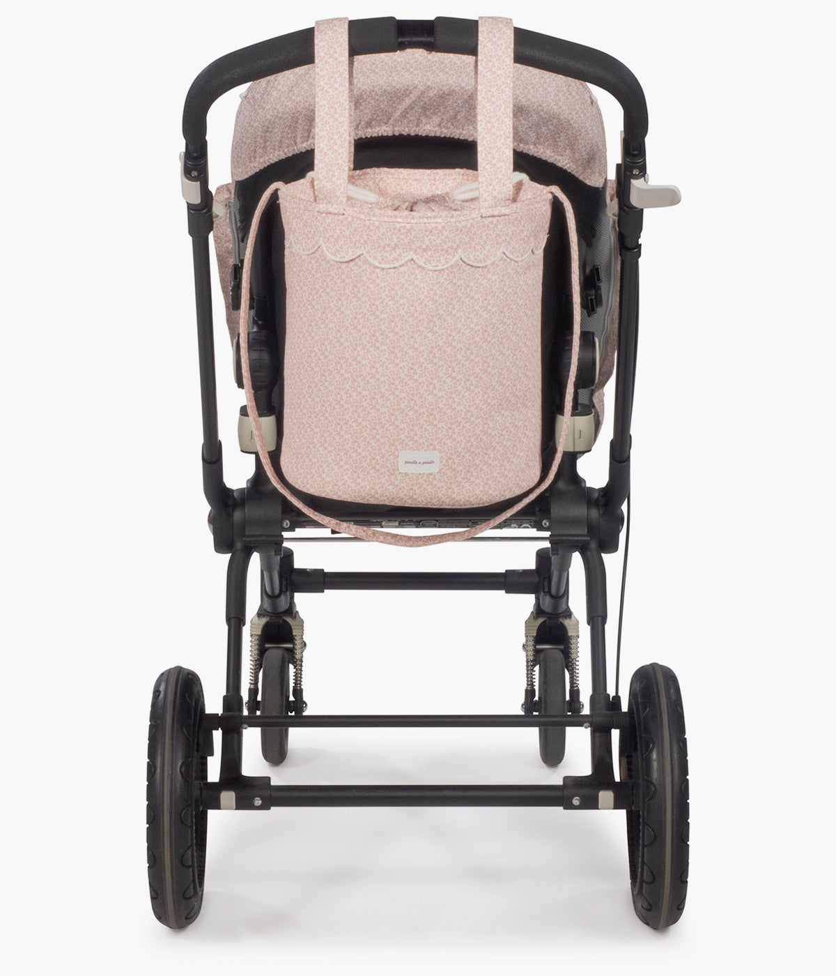 Vista pendurada no carrinho da bolsa bucket Maison Tender da Pasito a Pasito com o padrão flores. Elegante bolsa que combina um formato compacto e funcional com o delicado padrão de flores rosa da coleção. Fabricada em algodão BCI com tratamento resistente à água, possui forro interior em poliéster, fecho superior por cordão ajustável e espaço para transportar os principais essenciais da bebé. Inclui alças adicionais para prender ao carrinho e uma alça comprida para transportar ao ombro.