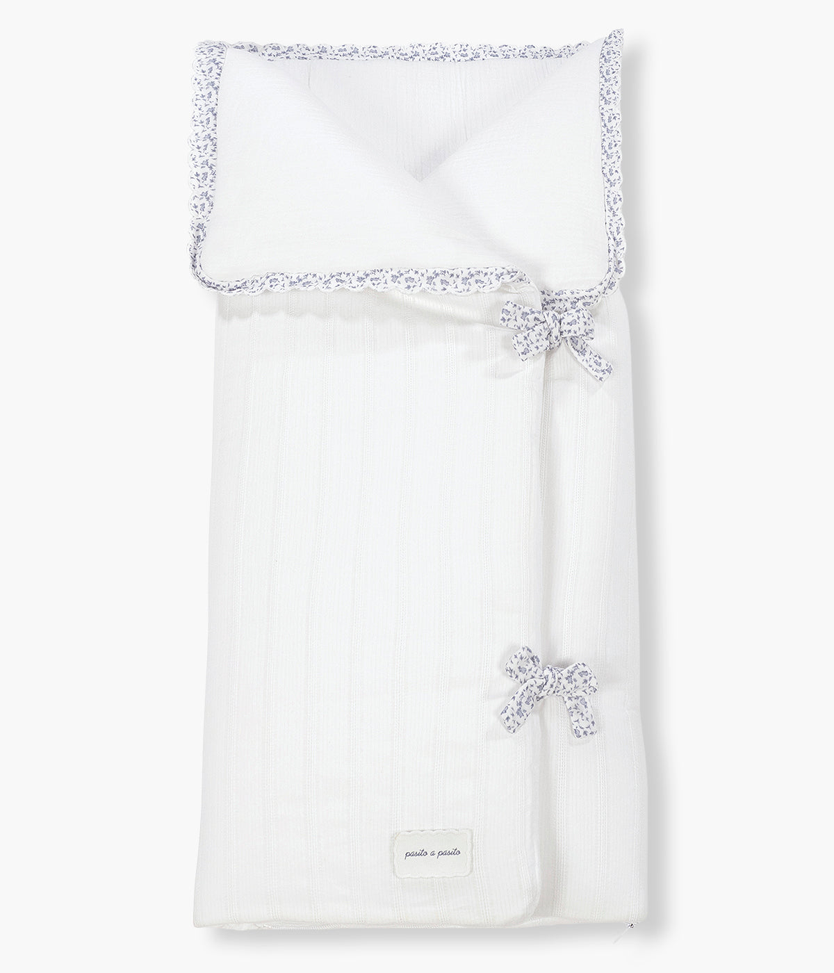 Vista frontal do saco Manta Maison Tender da Pasito a Pasito. Elegante saco manta com TOG 2.5 que proporciona uma envolvência suave e confortável nos primeiros meses do bebé. Fabricado em 100% algodão, combina um exterior branco com delicada textura de riscas verticais e um interior em musselina lisa de algodão. O formato tipo envelope, os laços de ajuste e o fecho de correr na zona dos pés ajudam a manter o bebé aconchegado, podendo ainda ser completamente aberto e utilizado como manta.