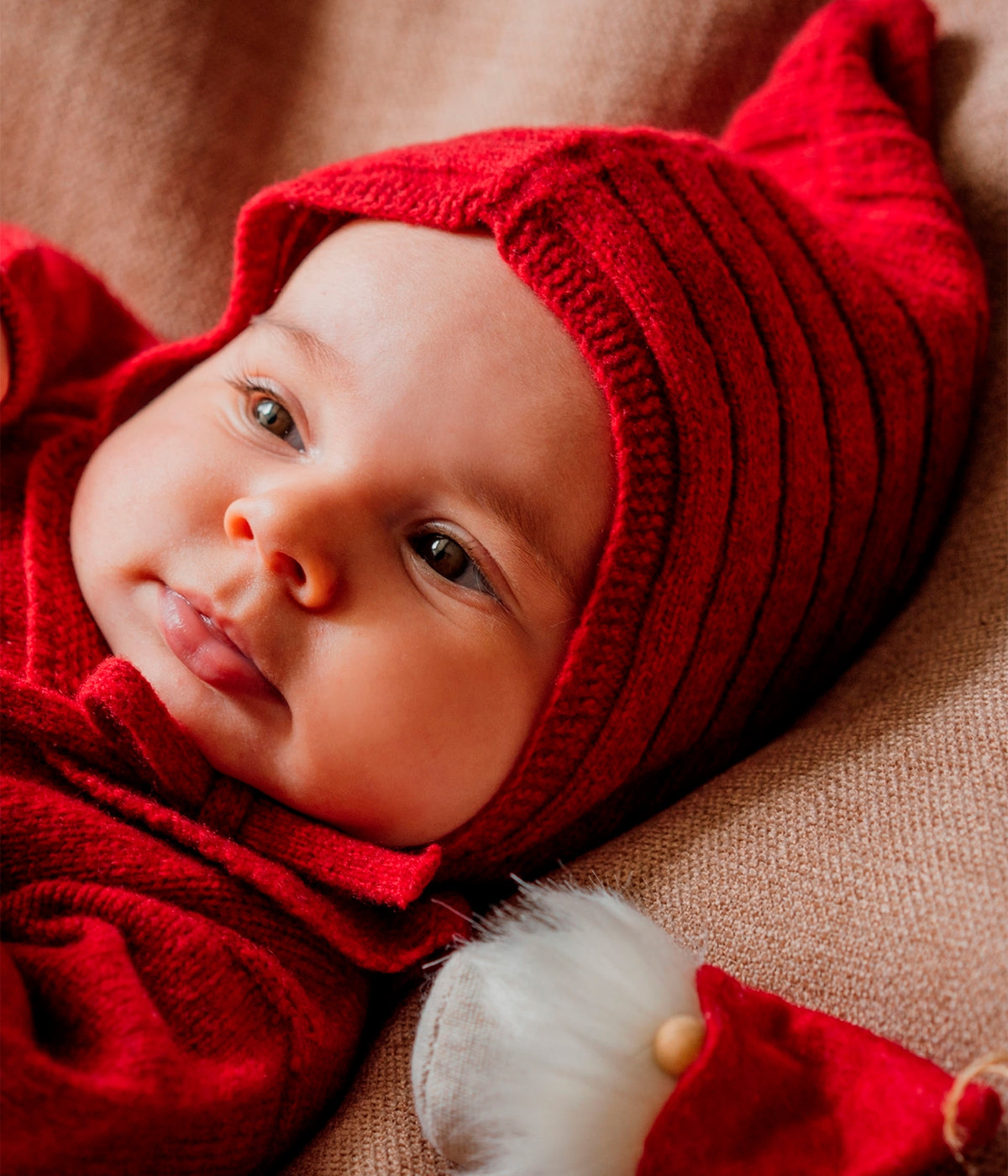 Bebé a usar a touca tricotada em lã merino extrafina vermelho-escuro da Wedoble para bebé e recém-nascido(a). Elegante touca sem costuras no interior com cordões para atar no queixo.