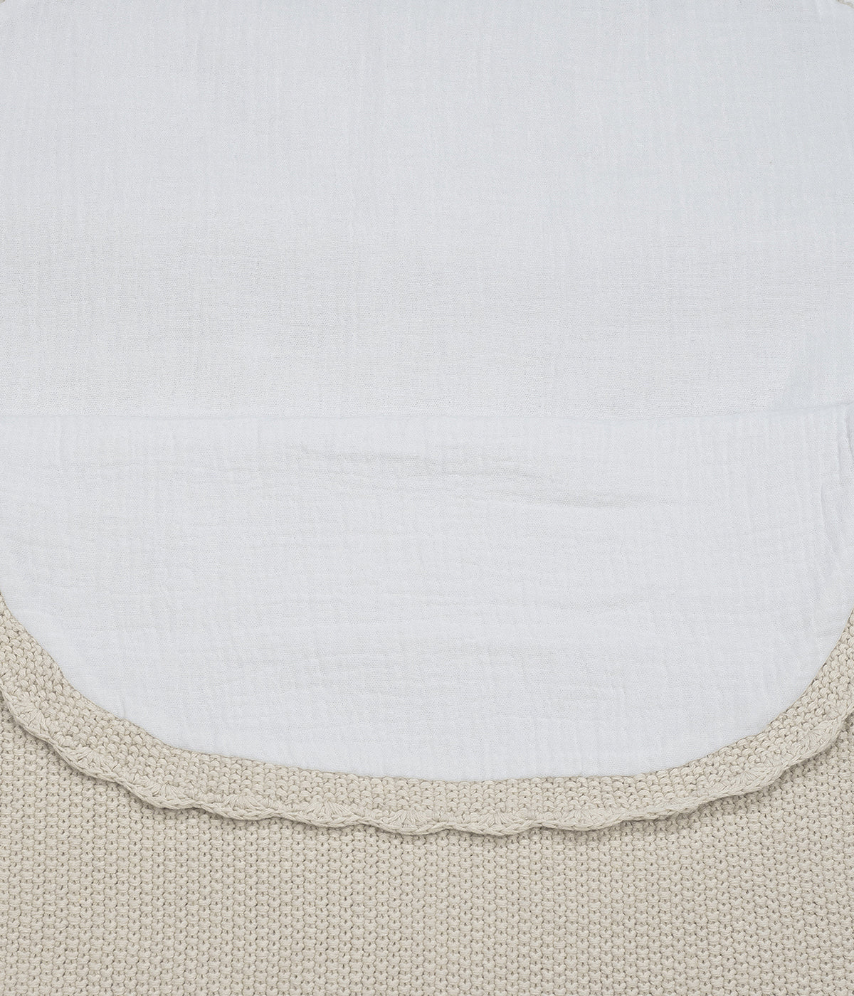Saco manta em malha de algodão tricot bege da Pasito a Pasito para bebé e recém-nascido(a). Este suave saco manta destaca-se pelo seu ponto de arroz requintado e um elegante acabamento com rebordo ondulado. Possui um design funcional com um interior em tecido musselina branco, permitindo ser utilizado como ninho ou como manta de berço, acompanhando o crescimento e as diferentes necessidades do bebé.