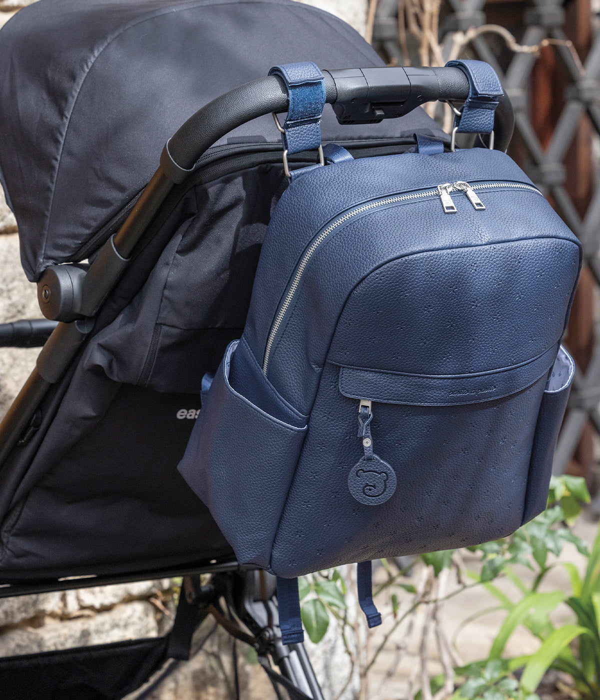 Mochila de Maternidade Pasito a Pasito New London Blue em polipele de cor azul-marinho pendurada no carrinho.