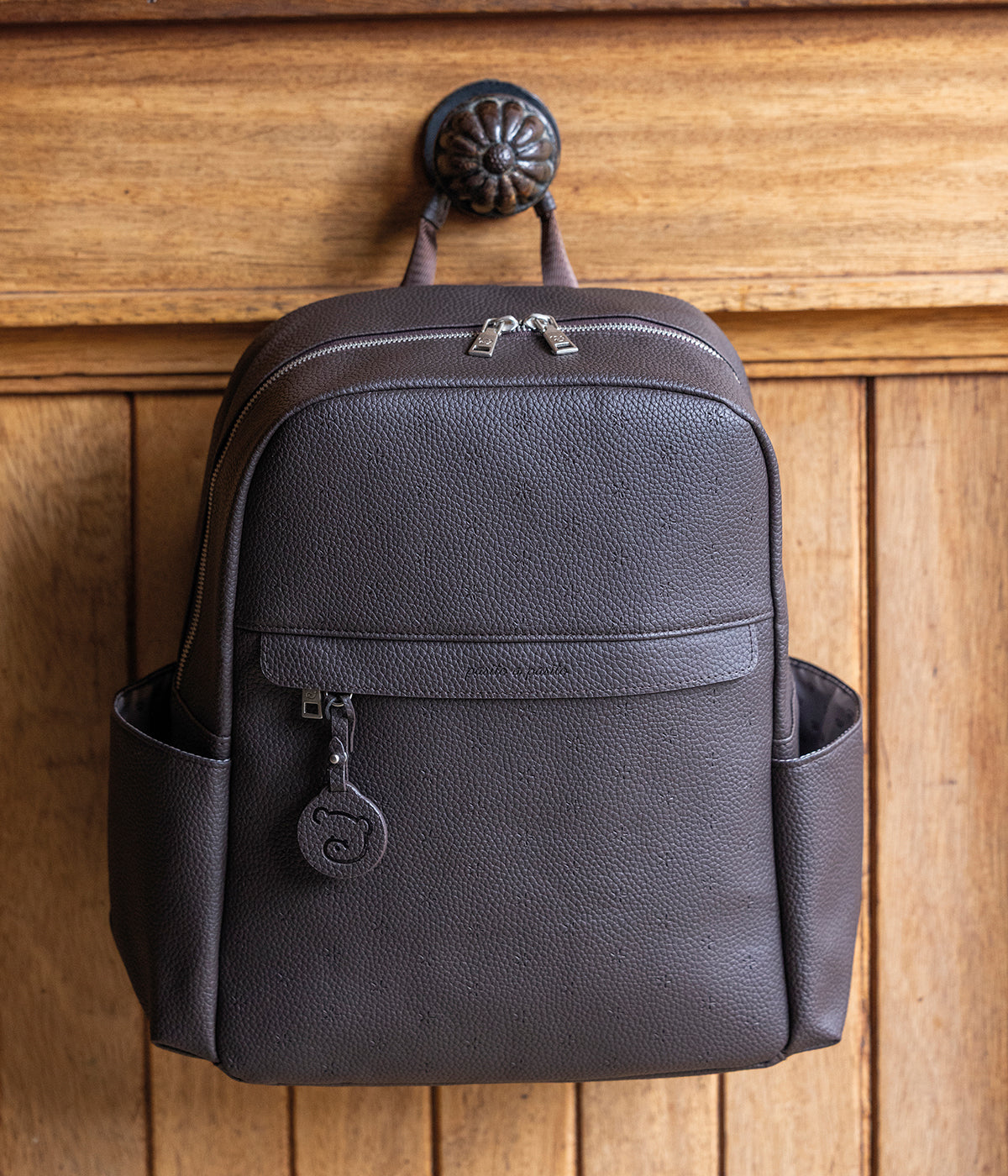 Mochila de Maternidade Pasito a Pasito New London Brown em polipele castanha de design elegante composto por um padrão estrelas com bolsos laterais, bolso frontal e diversos compartimentos no interior. Para transporte, esta mochila de maternidade dispõe de alças ajustáveis para usar às costas e pequenas alças menores para pendurar no carrinho do bebé.