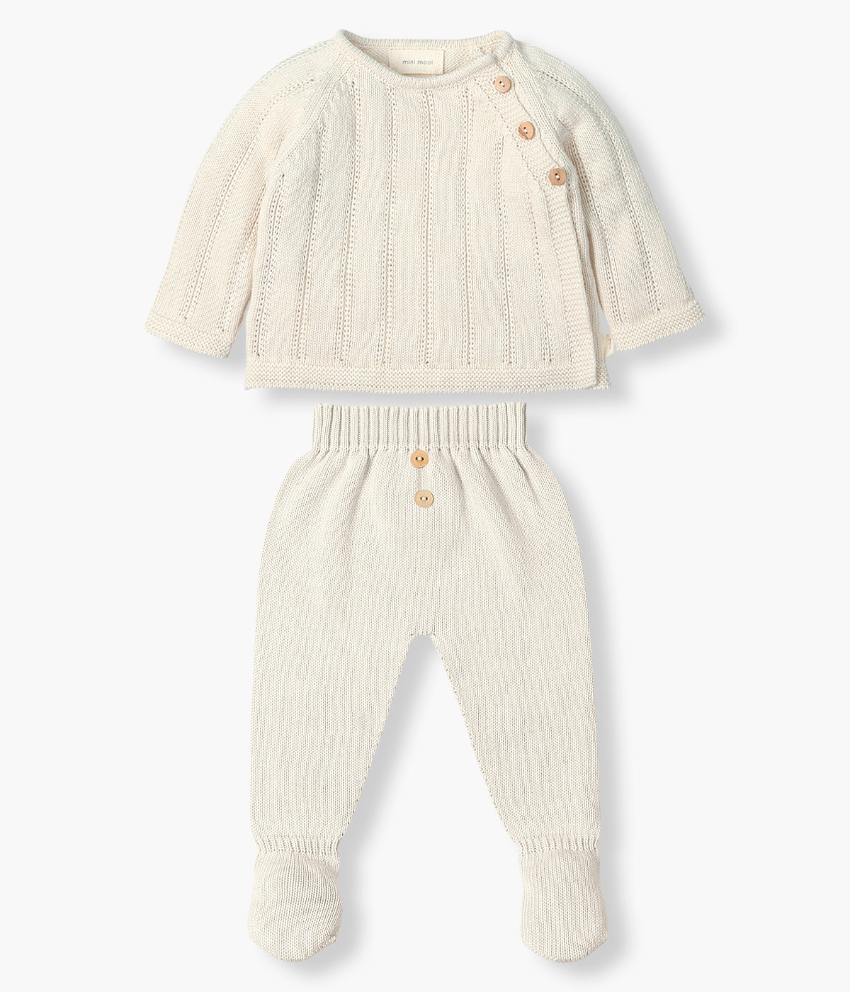 Vista de frente do conjunto em malha de algodão orgânico pérola da Mini Mooi para bebé e recém‑nascido(a), composto por camisola e calças. Camisola de manga comprida com detalhes entrelaçados na malha e abertura no ombro com botões de madeira. Calças lisas com pés com botões de madeira decorativos.