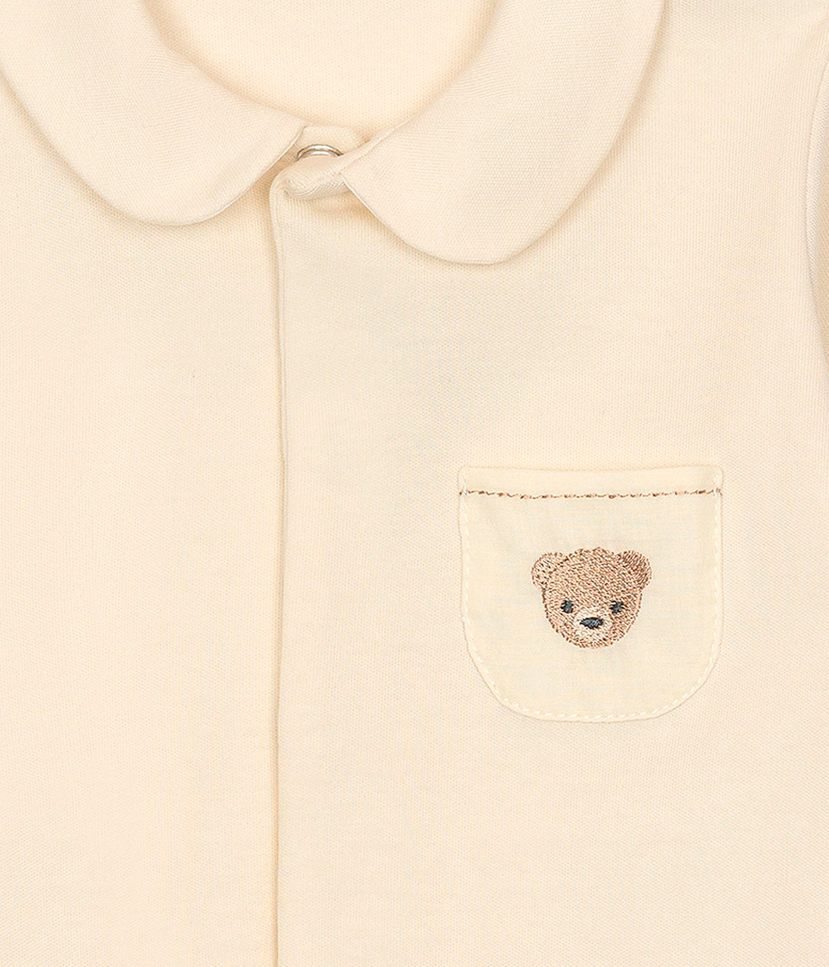Vista de frente do babygrow em algodão bege da Baby Gi para bebé e recém-nascido. Gola redonda cortada e bolso no peito com urso bordado em castanho. Abertura com molas de pressão na frente e entrepernas.