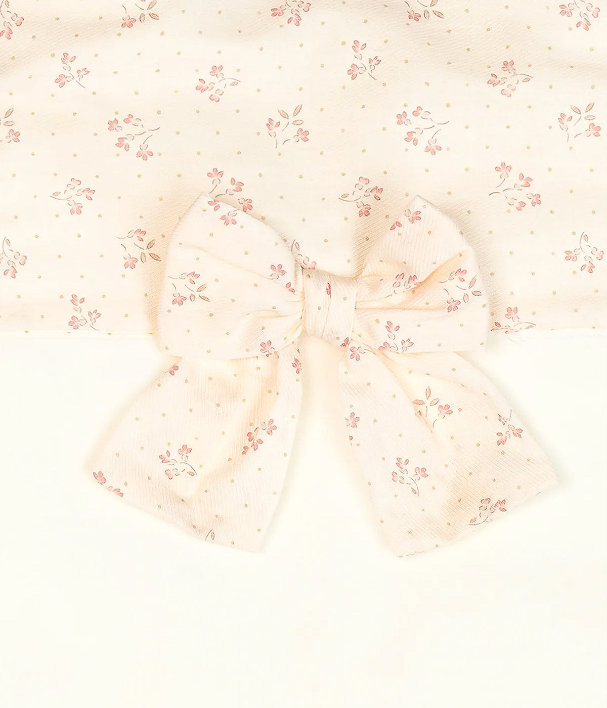 Vista detalhada da manta em veludo pérola da Baby Gi para bebé menina e recém-nascida. Quentinha manta com detalhe em tecido e laço rosa com padrão pequenas flores.
