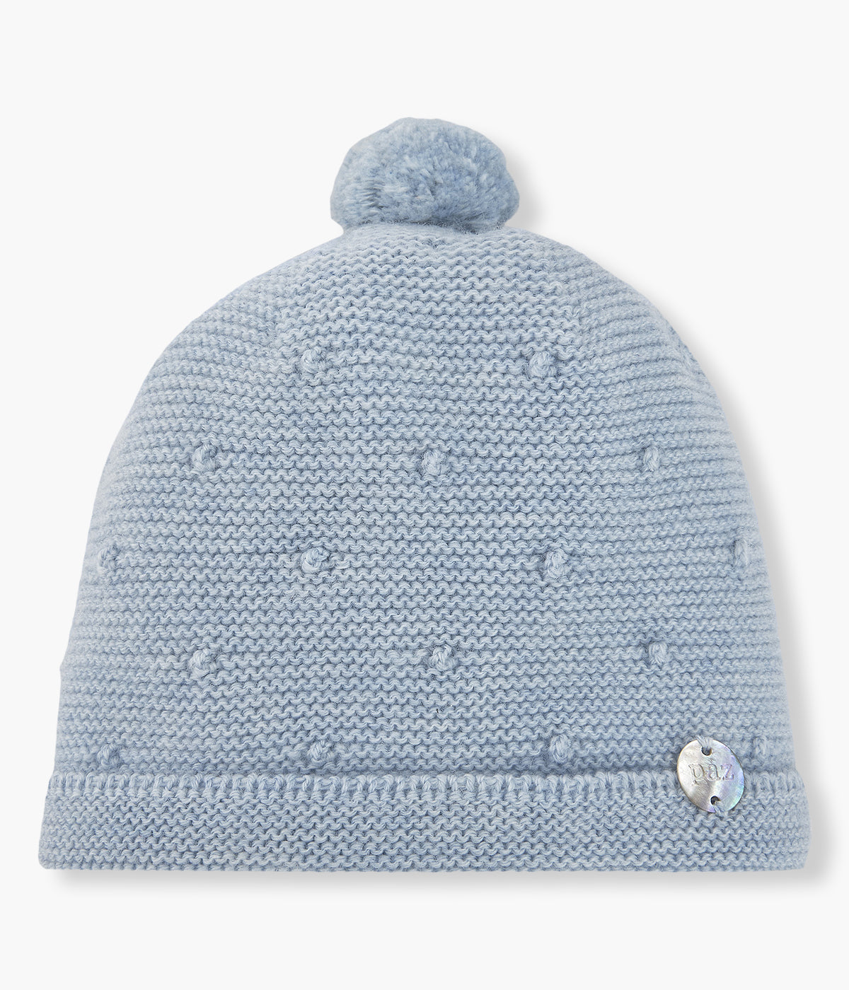 Gorro em malha azul da Paz Rodríguez para bebé e recém-nascido(a). Detalhes com relevo, pequena medalha madrepérola com logo da marca e pompom.