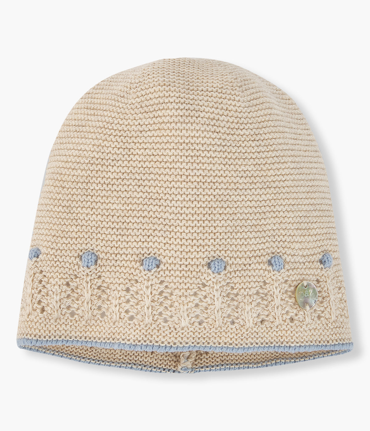 Gorro em malha de algodão com caxemira bege da Paz Rodríguez para bebé e recém-nascido(a). Detalhes em azul com relevo e pequena medalha madrepérola com logo da marca.