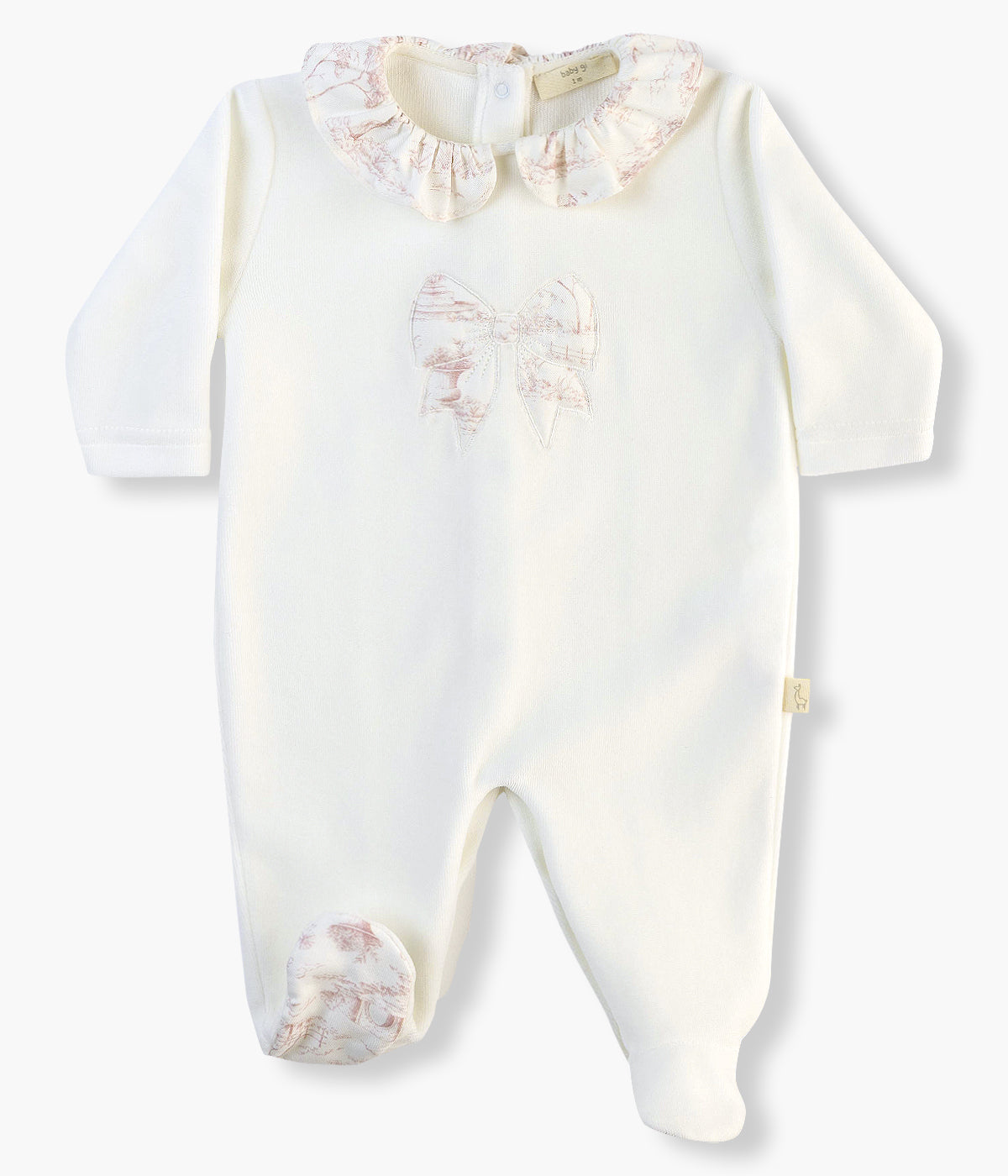 Babygrow em veludo pérola da Baby Gi para bebé menina e recém-nascida. Gola folho, laço no peito e planta do pé com aplicação em tecido de padrão toile de jouy cor-de-rosa. Abertura nas costas e entrepernas.