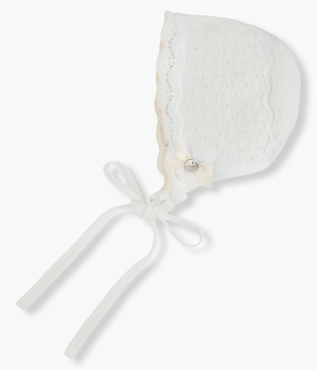 Touca em malha de algodão pérola da Paz Rodríguez para bebé menina e recém-nascida. Detalhes com relevo, contornos ondulados e laço com medalha madrepérola.