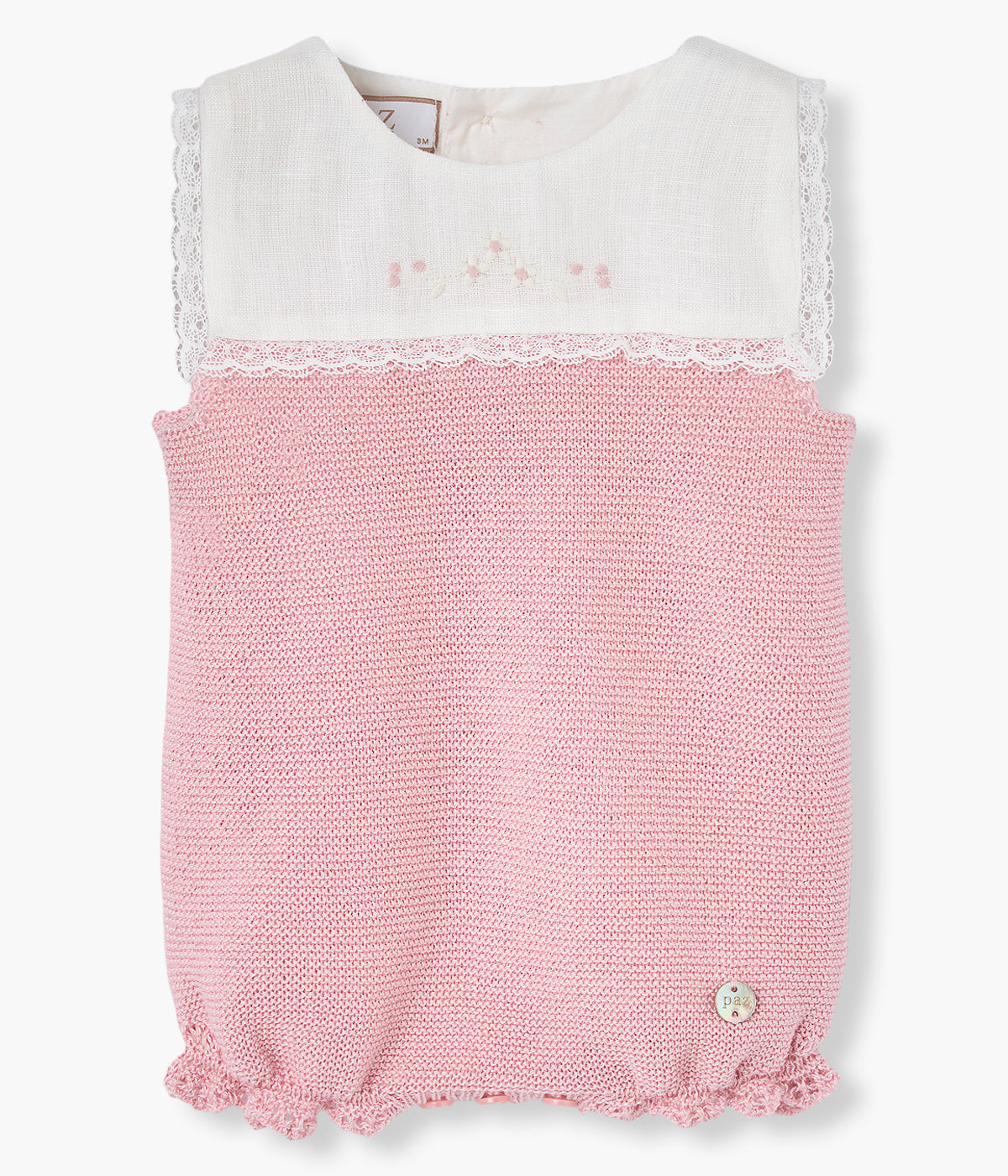 Vista de frente do fofo em malha de algodão sem mangas da Paz Rodríguez para bebé menina e recém-nascida. Parte superior com peitilho em tecido branco com bordado floral e contornos com renda. Parte inferior em malha de algodão rosa-velho com detalhes nos contornos inferiores. Abertura nas costas e entrepernas.