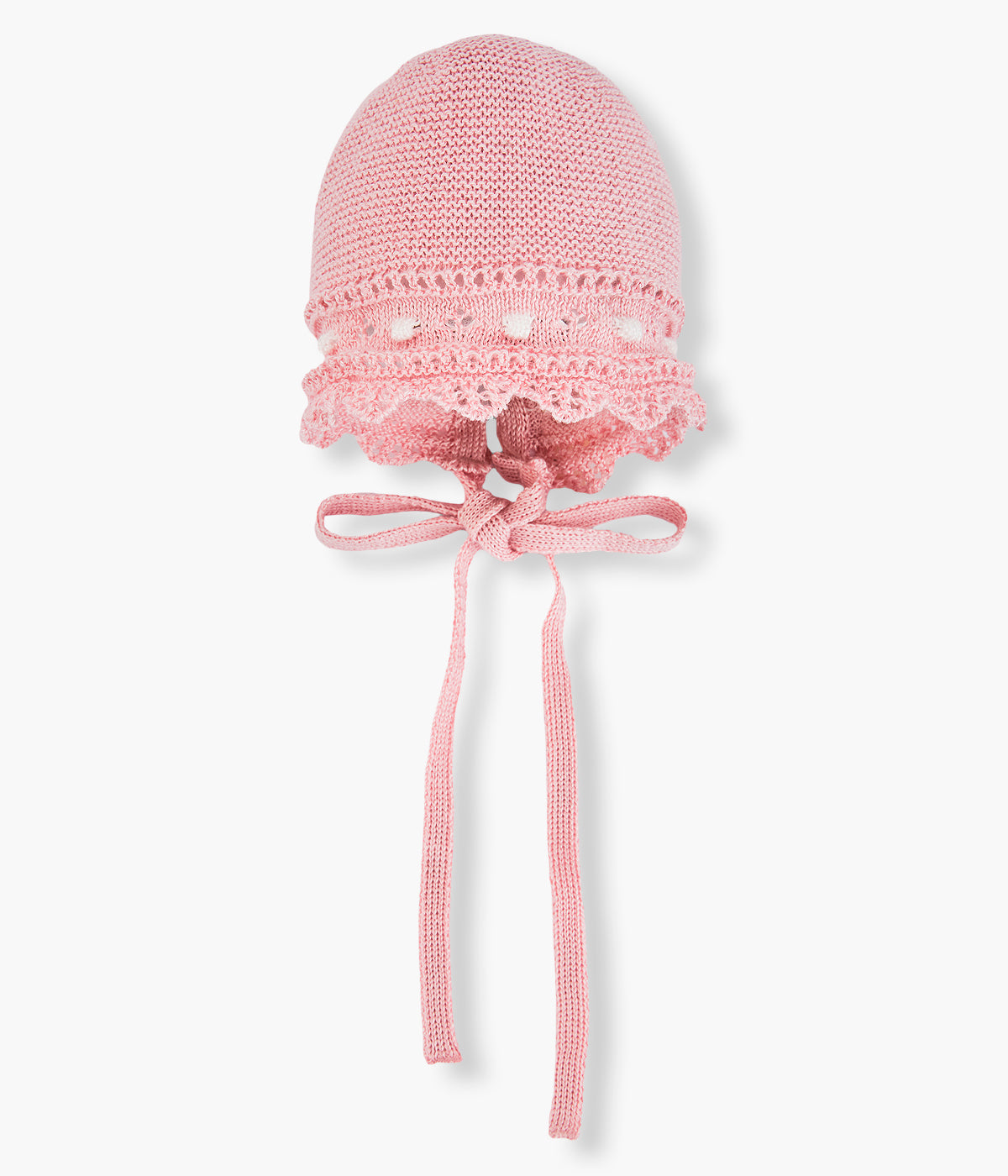 Vista de frente da touca em malha de algodão rosa-velho da Paz Rodríguez para bebé menina e recém-nascida. Detalhes com relevo em branco, contornos ondulados e laço com medalha madrepérola.