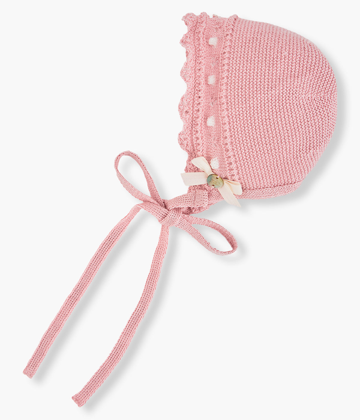 Vista de lado da touca em malha de algodão rosa-velho da Paz Rodríguez para bebé menina e recém-nascida. Detalhes com relevo em branco, contornos ondulados e laço com medalha madrepérola.