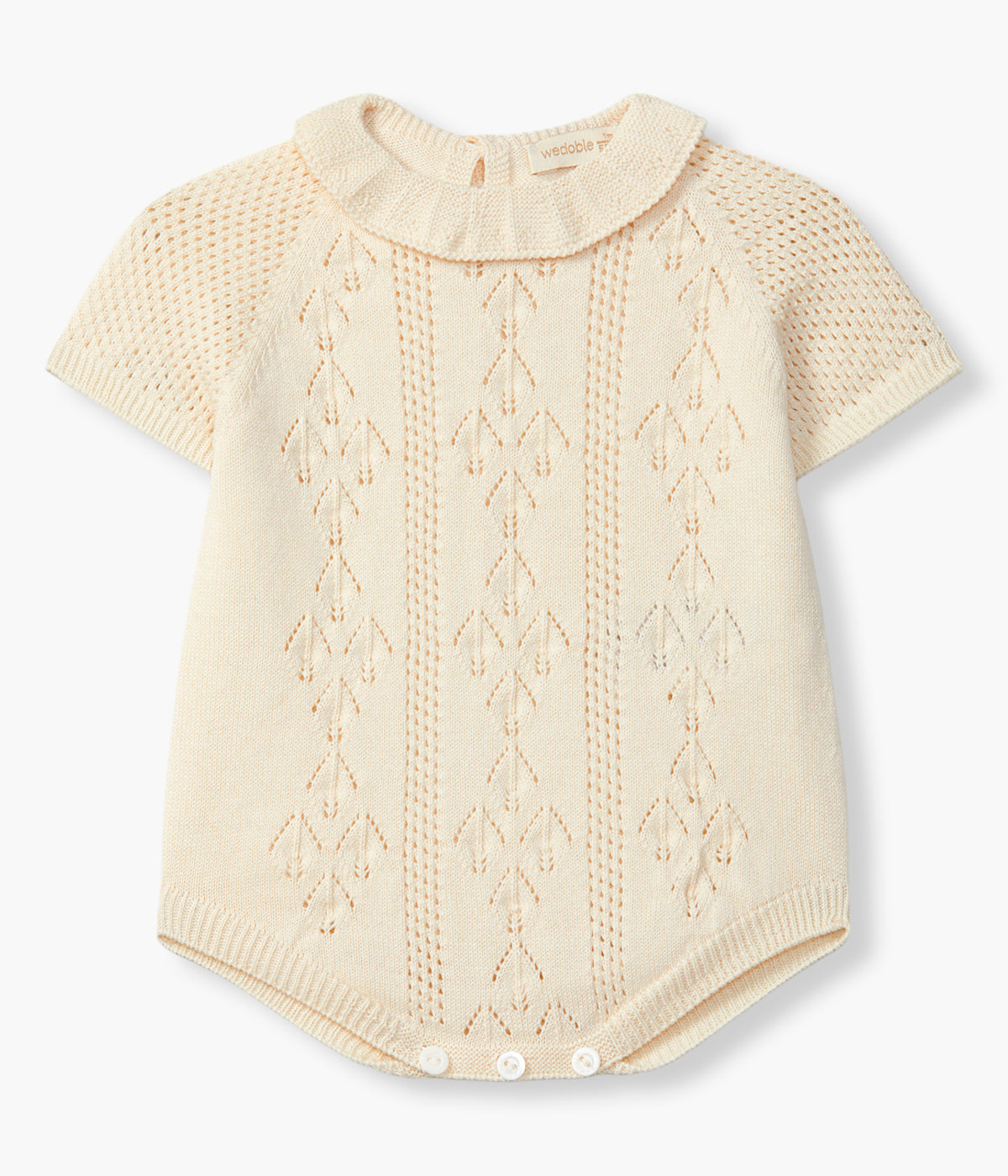 Vista de frente do fofo em malha de algodão orgânico bege da Wedoble para bebé e recém-nascido(a). Suave e delicada malha com detalhes perfurados na frente e gola folho. Abertura nas costas e entrepernas.