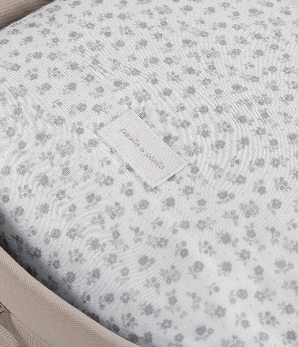Vista na alcofa do saco de dormir Little Bloom Flowers da Pasito a Pasito. Delicado saco de dormir para alcofa que envolve a bebé em conforto e suavidade desde os primeiros passeios. Criado com tecido 100% algodão, combina muselina com padrão floral cinza, um interior liso com enchimento removível e colchão interior com tecido 3D para maior ventilação.