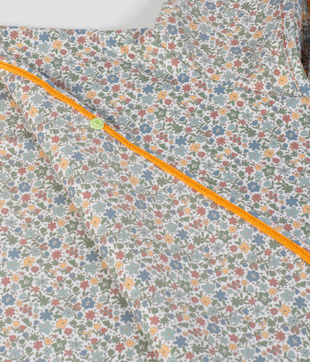 Vista detalhada do poncho de microfibra Summer Flowers da Walking Mum. Peça ideal para depois do banho na praia ou piscina, este poncho com padrão floral é leve, suave e de secagem rápida. Envolve a bebé com conforto e proteção solar FPS/SPF 50+, garantindo bem-estar e segurança.