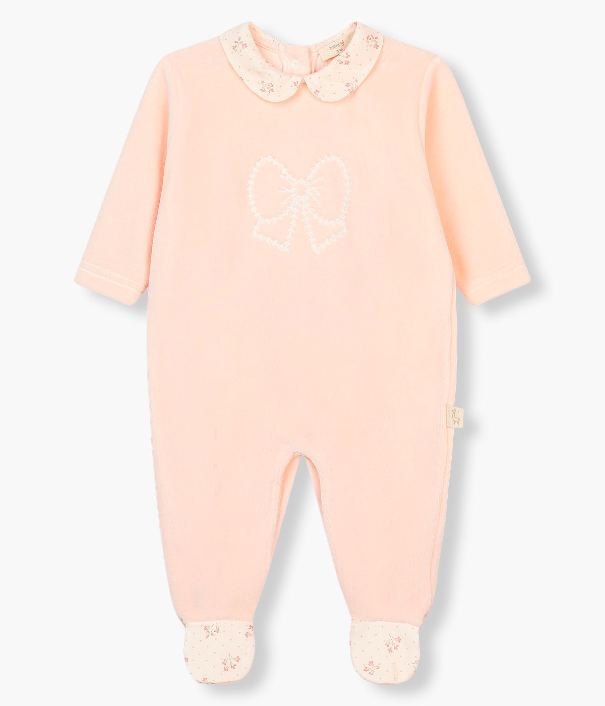 Vista frontal do babygrow em veludo rosa da Baby Gi para bebé menina e recém-nascida. Gola redonda cortada e pés com padrão pequenas flores. Laço bordado no peito. Abertura nas costas e entrepernas.
