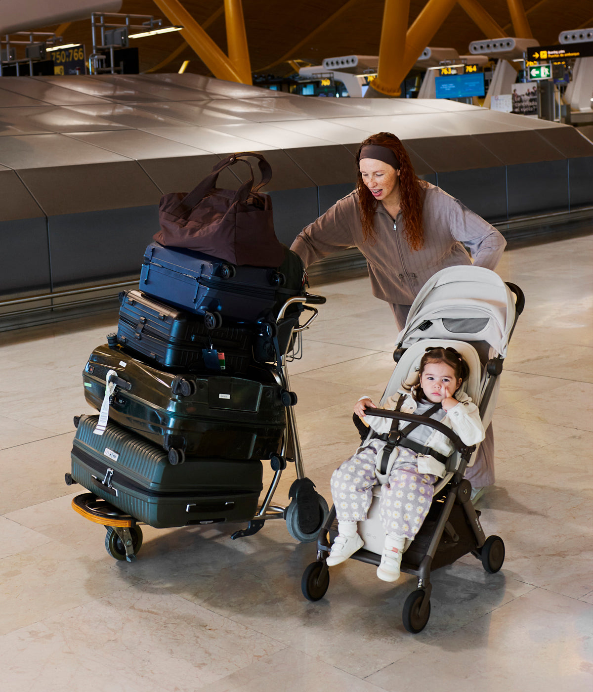 Mae a empurar carrinho de passeio Air-Q e malas de viagem.