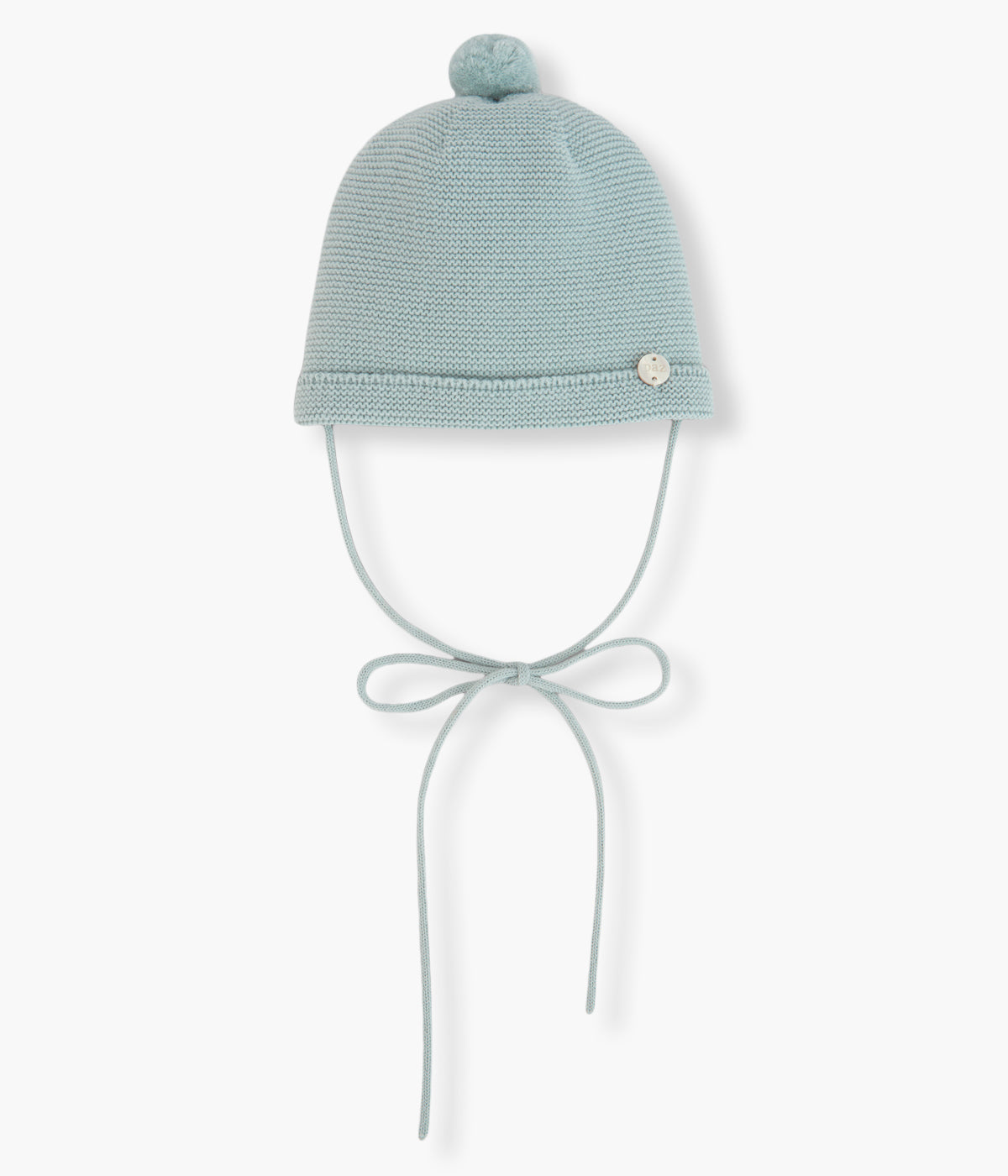 Vista frontal do gorro de malha verde-água da Paz Rodríguez para bebé e recém-nascido(a). Quentinho gorro com pompom no topo, dobra com medalha madrepérola e tiras para atar no queixo.