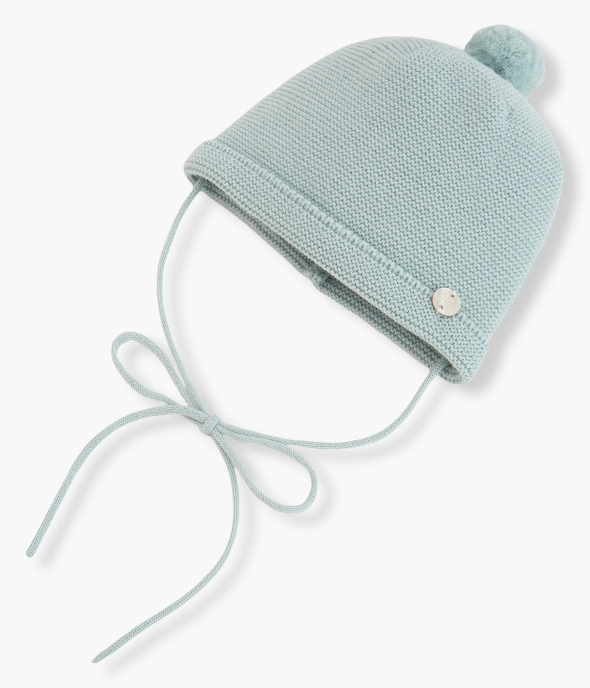 Vista frontal do gorro de malha verde-água da Paz Rodríguez para bebé e recém-nascido(a). Quentinho gorro com pompom no topo, dobra com medalha madrepérola e tiras para atar no queixo.