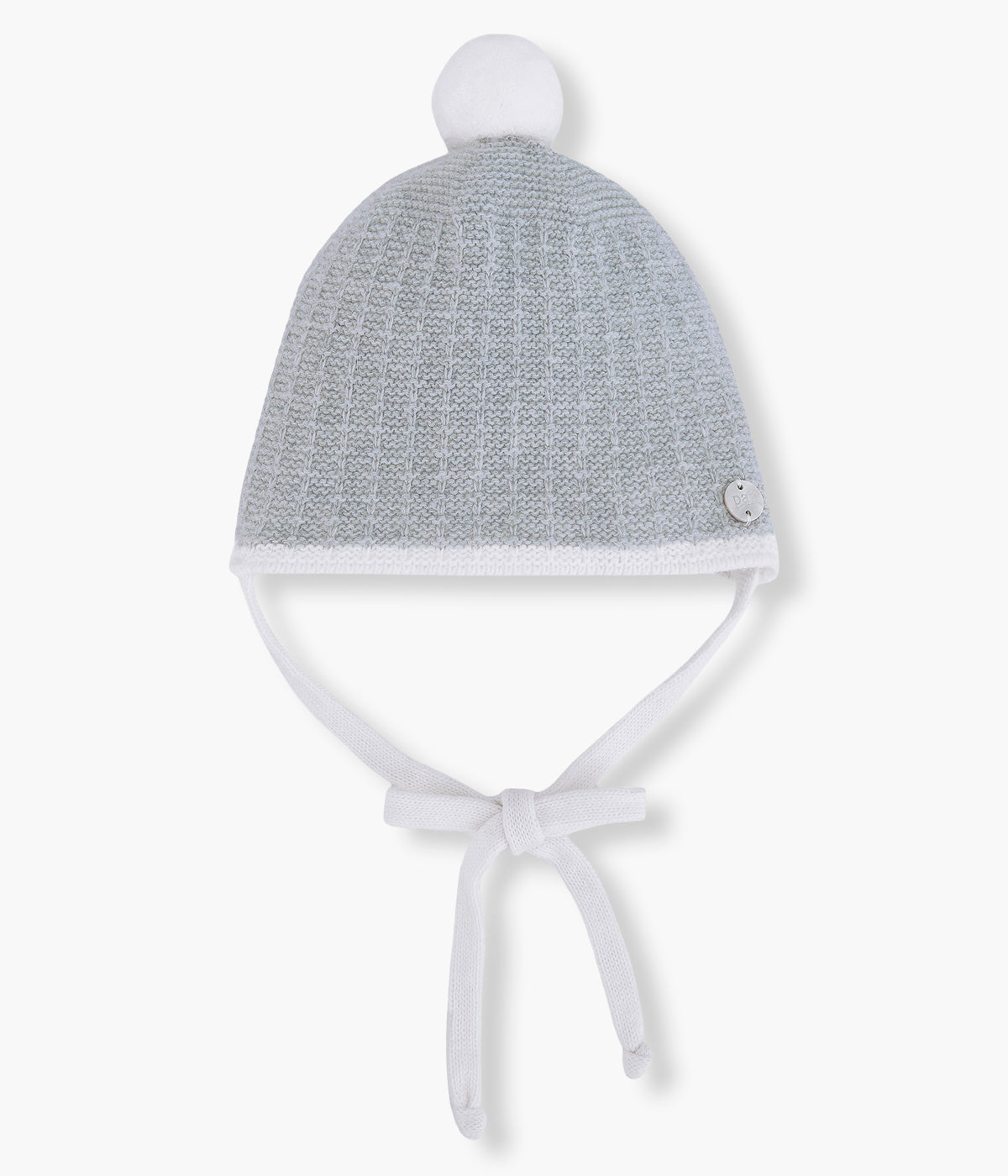 Vista frontal do gorro em malha de lã e caxemira cinza da Paz Rodríguez para bebé e recém-nascido(a). Pompom e tiras em branco para atar no queixo. Medalha da marca em madrepérola.