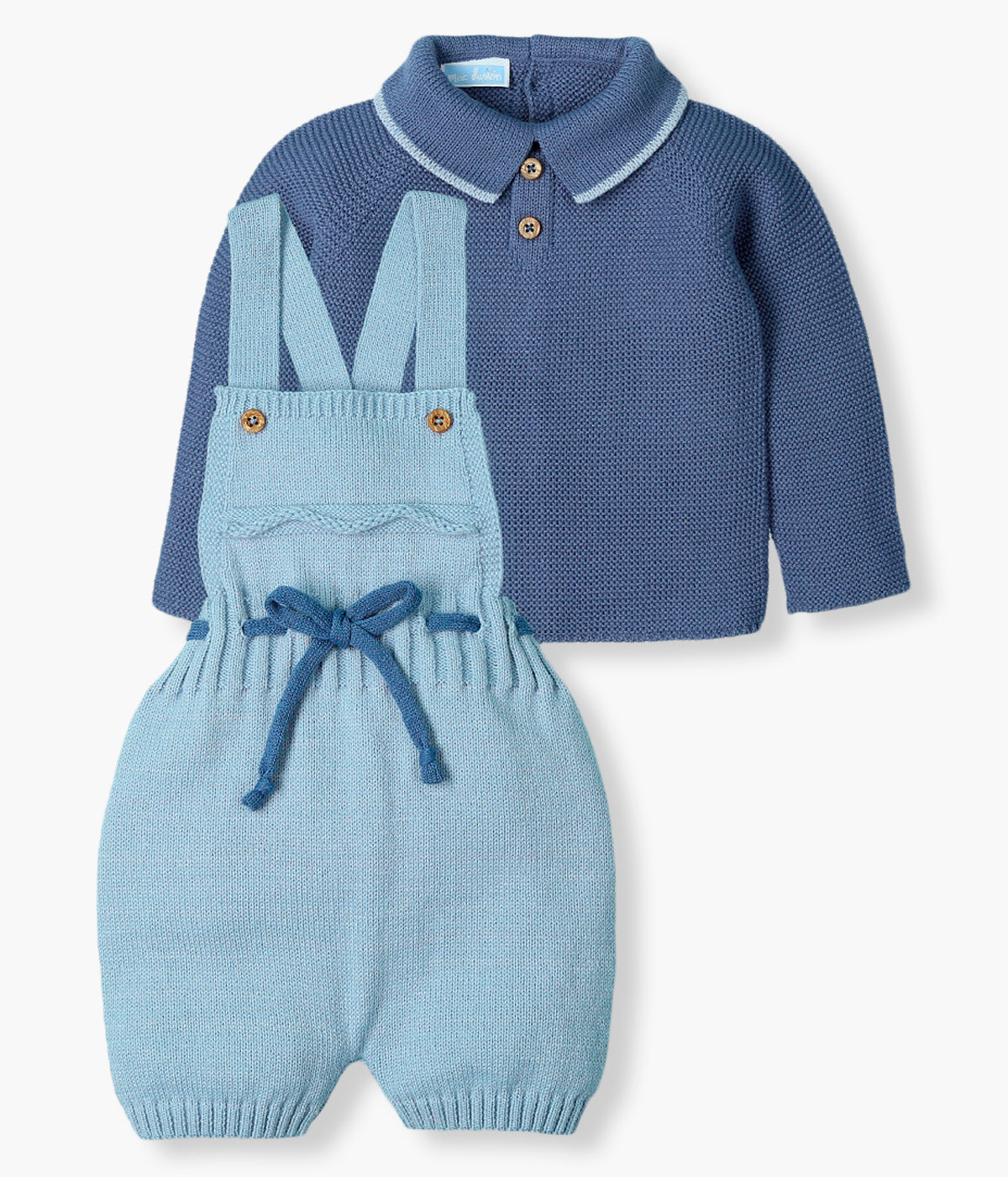 Vista frontal do conjunto de 2pc em malha da Mac Ilusión para bebé menino e recém-nascido. Camisola azul-escura com gola bico cortada com contorno em azul e dois botões decorativos. Macacão de alças com detalhe no peito e cordão a combinar com a camisola. Abertura da camisola nas costas e abertura do macacão nas alças.