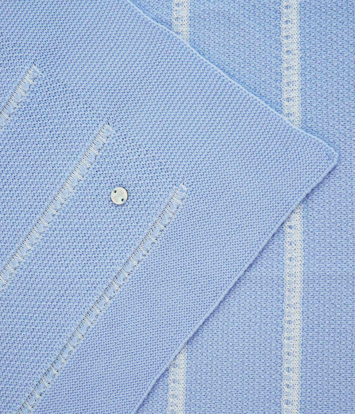 Vista detalhada da manta de malha azul da Paz Rodríguez para bebé e recém-nascido(a). Suave manta de formato retangular com medalha madrepérola da marca e detalhes em branco.