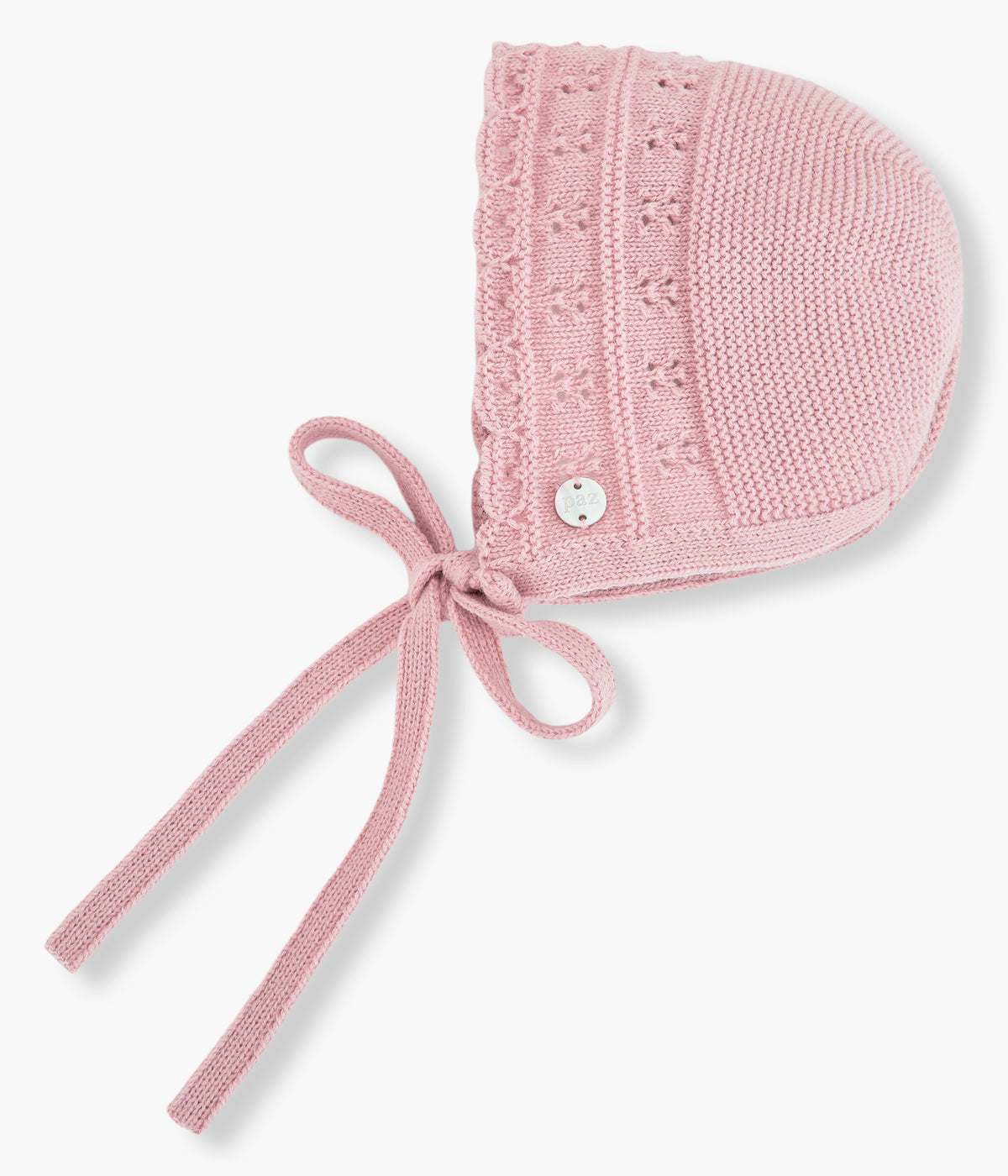 Vista lateral da touca de malha rosa da Paz Rodríguez para bebé menina e recém-nascida. Suave touca com detalhes com relevo, medalha de madrepérola e tiras para atar no queixo.