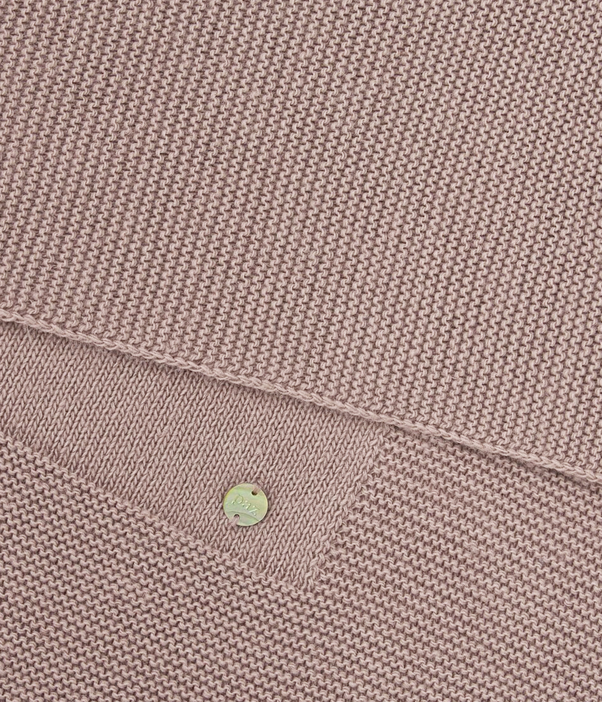 Vista detalhada da manta de malha bege da Paz Rodríguez para bebé e recém-nascido(a). Suave manta de formato retangular com medalha madrepérola da marca.