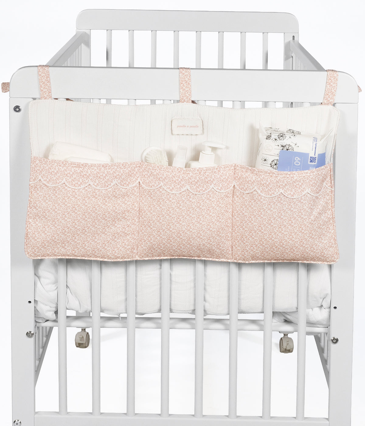 Vista aplicada no berço do organizador de berço Maison Tender da Pasito a Pasito com o padrão floral rosa. Perfeito para manter os essenciais da bebé sempre organizados e facilmente acessíveis junto ao berço.