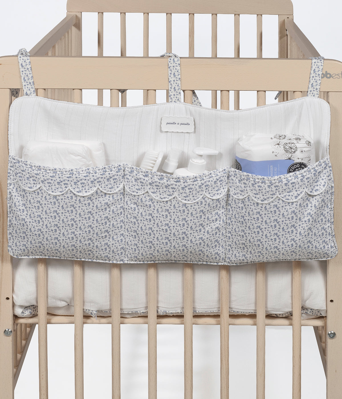 Vista aplicada no berço do organizador de berço Maison Tender da Pasito a Pasito com o padrão coelhos azuis. Perfeito para manter os essenciais do bebé sempre organizados e facilmente acessíveis junto ao berço.