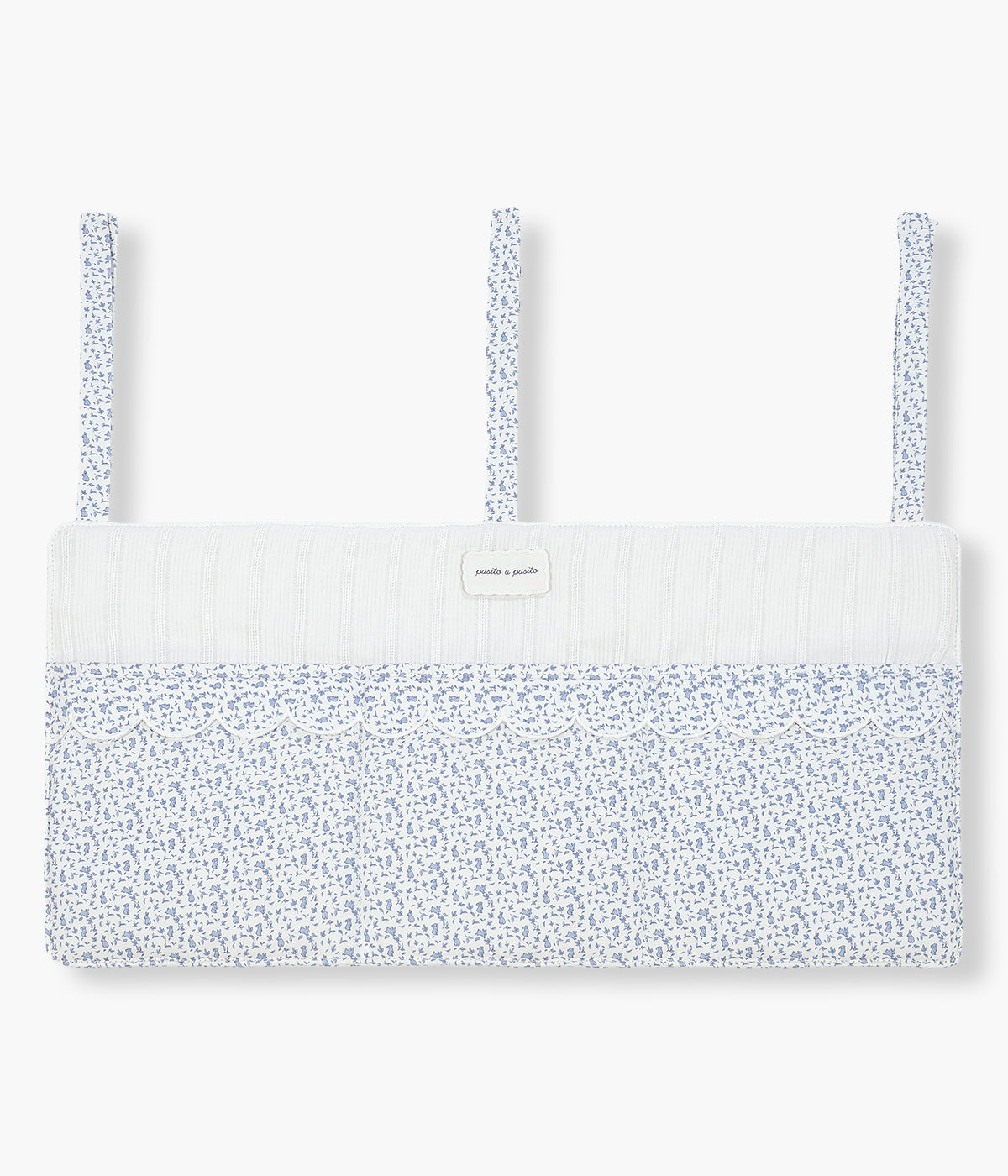 Vista frontal do organizador de berço Maison Tender da Pasito a Pasito com o padrão coelhos azuis. Perfeito para manter os essenciais do bebé sempre organizados e facilmente acessíveis junto ao berço. Fabricado em algodão, possui bolsos amplos e estruturados para fraldas, musselinas, chupetas e pequenos acessórios, fixando-se facilmente através de fitas ajustáveis. O delicado padrão de coelhinhos completa o ambiente com o estilo suave e elegante da coleção Maison Tender.