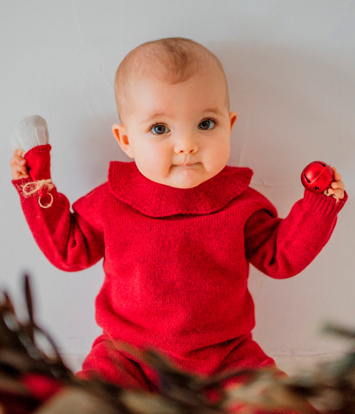 Bebé a vestir o babygrow tricotado em lã merino extrafina vermelho-escuro da Wedoble.
