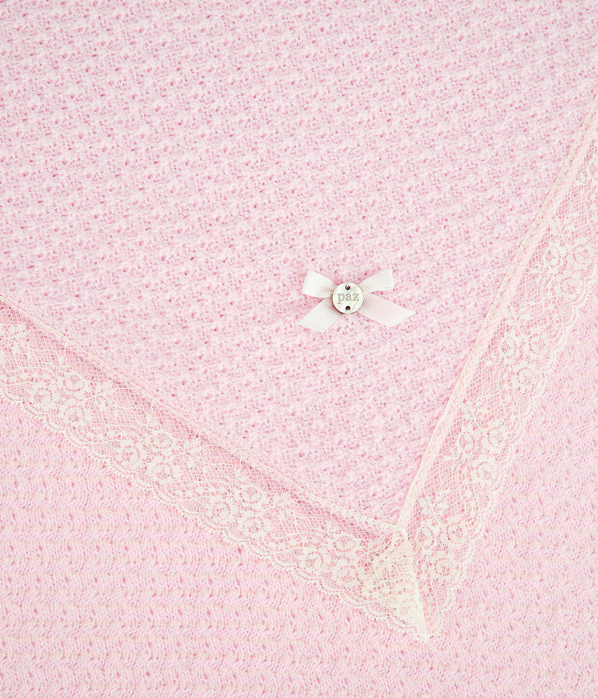 Vista detalhada da manta de malha rosa da Paz Rodríguez para bebé menina e recém-nascida. Suave manta de malha detalhada de formato quadrado com contorno em renda bege e medalha de madrepérola com pequeno laço.