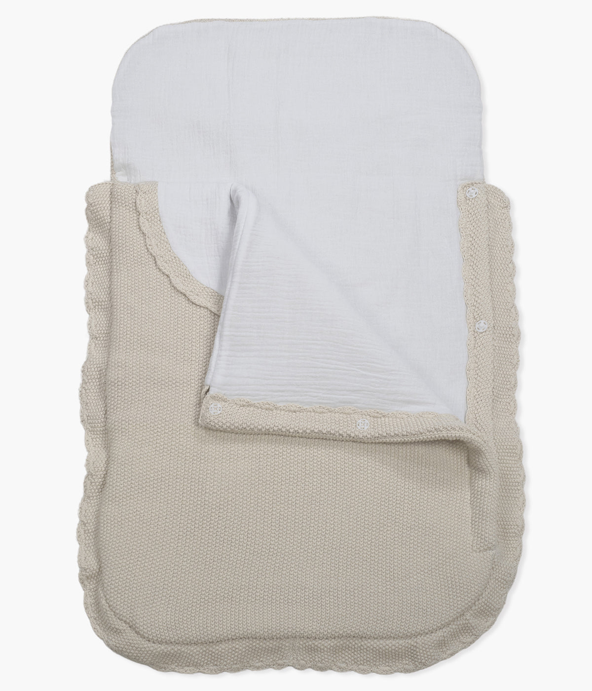 Saco manta em malha de algodão tricot bege da Pasito a Pasito para bebé e recém-nascido(a). Este suave saco manta destaca-se pelo seu ponto de arroz requintado e um elegante acabamento com rebordo ondulado. Possui um design funcional com um interior em tecido musselina branco, permitindo ser utilizado como ninho ou como manta de berço, acompanhando o crescimento e as diferentes necessidades do bebé.