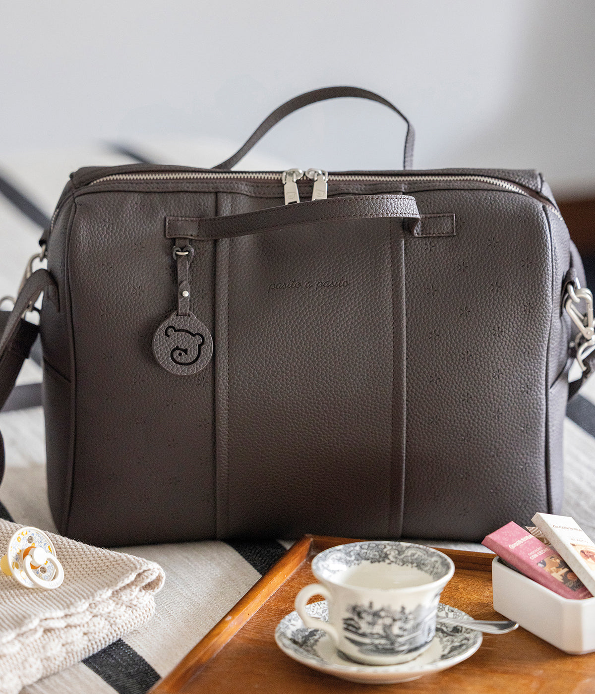 Mala de Maternidade Pasito a Pasito New London Brown em polipele castanha de design elegante composto por um padrão estrelas, essencial para acompanhar os primeiros anos do bebé. Com um design moderno e uma organização interior inteligente, garante que tudo o que é importante está sempre à mão, mantendo um toque de elegância em qualquer ocasião.