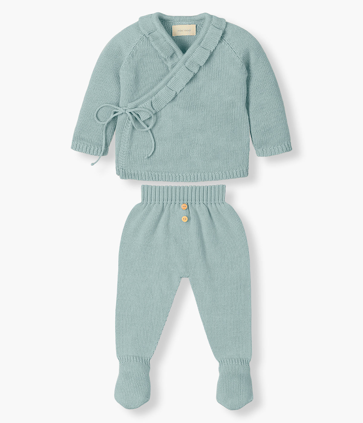Conjunto em malha de algodão orgânico verde da Mini Mooi para bebé menina e recém‑nascida, composto por camisola e calças. Camisola de manga comprida abertura trespasse com detalhe de folho na gola e abertura. Calças lisas com pés com botões de madeira decorativos.