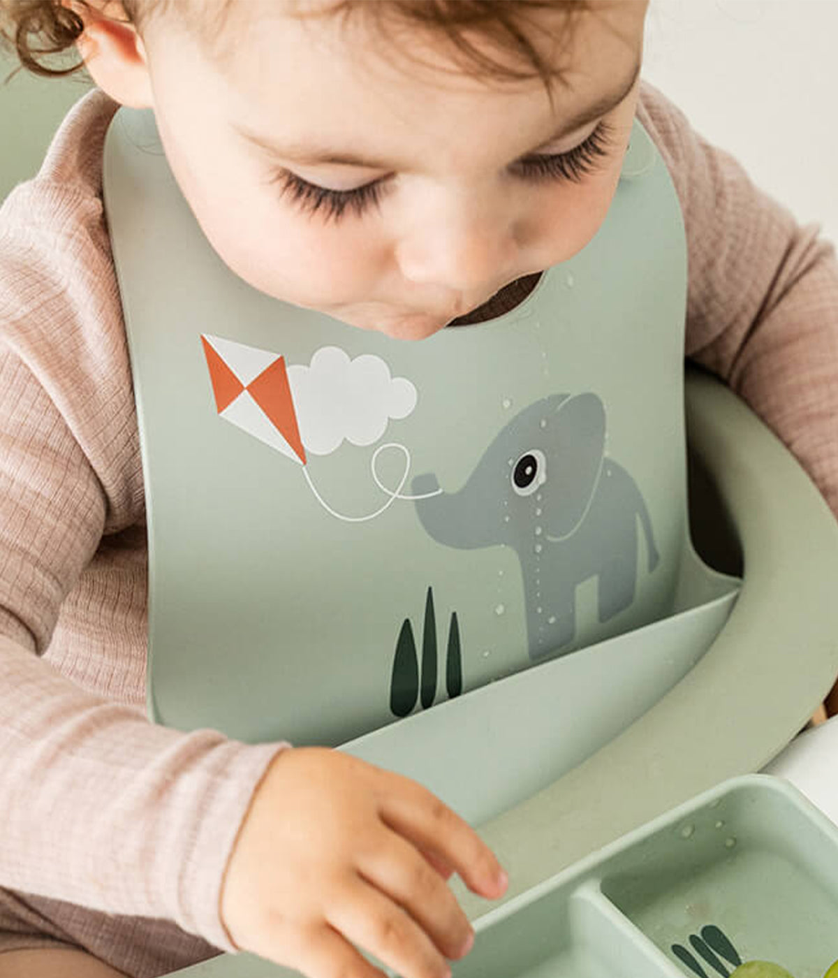 Bebé a usar a babete em silicone de grau alimentar verde Done By Deer decorada com oelefante Elphee.