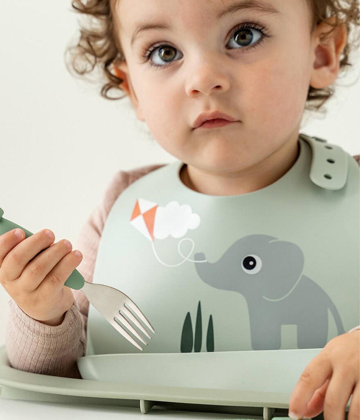 Bebé a usar a babete em silicone de grau alimentar verde Done By Deer decorada com o elefante Elphee.